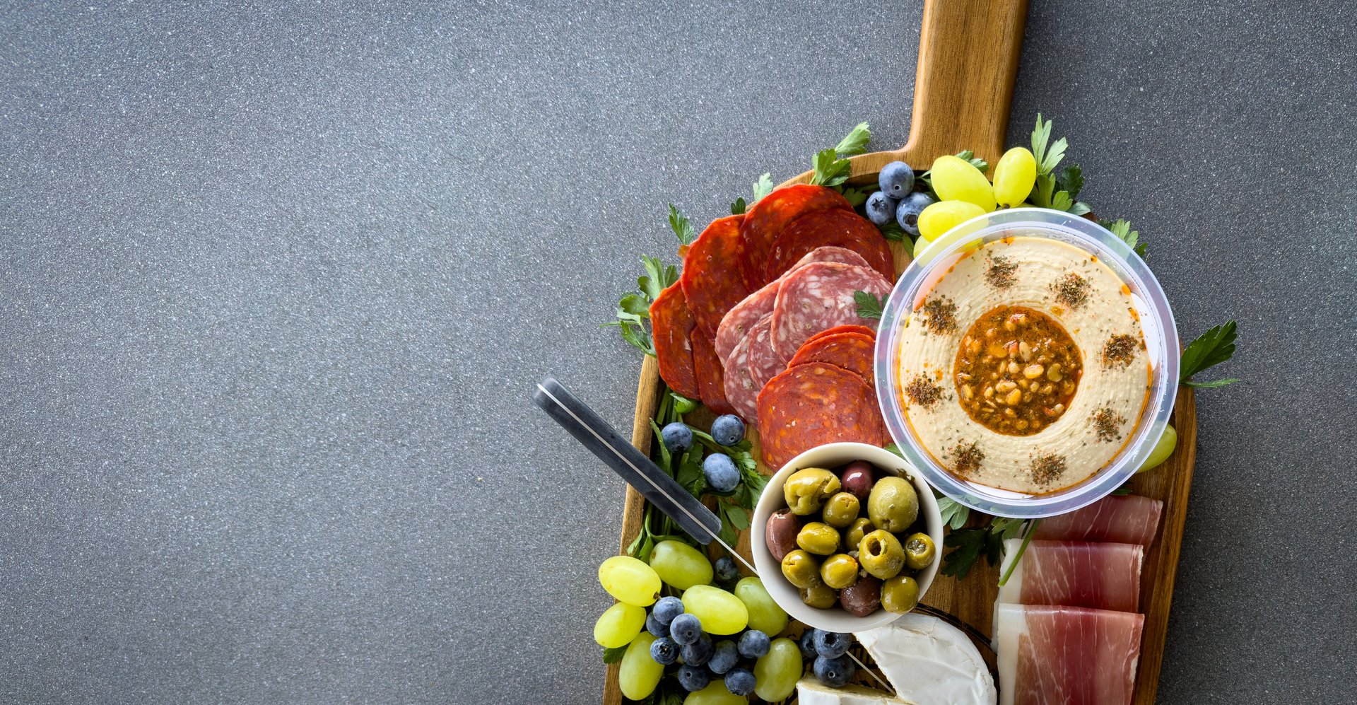 Top view of a gourmet charcuterie board or cheese platter with various meats, fruits and cheese on a wooden board in panoramic banner format