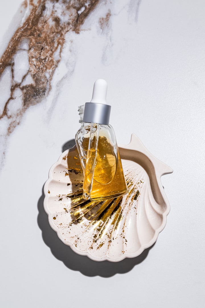 An open bottle of serum, a pipette filled with a cosmetic product. Hyaluronic acid, panthenol, gold 24K. Abstract marble background. top vertical view.