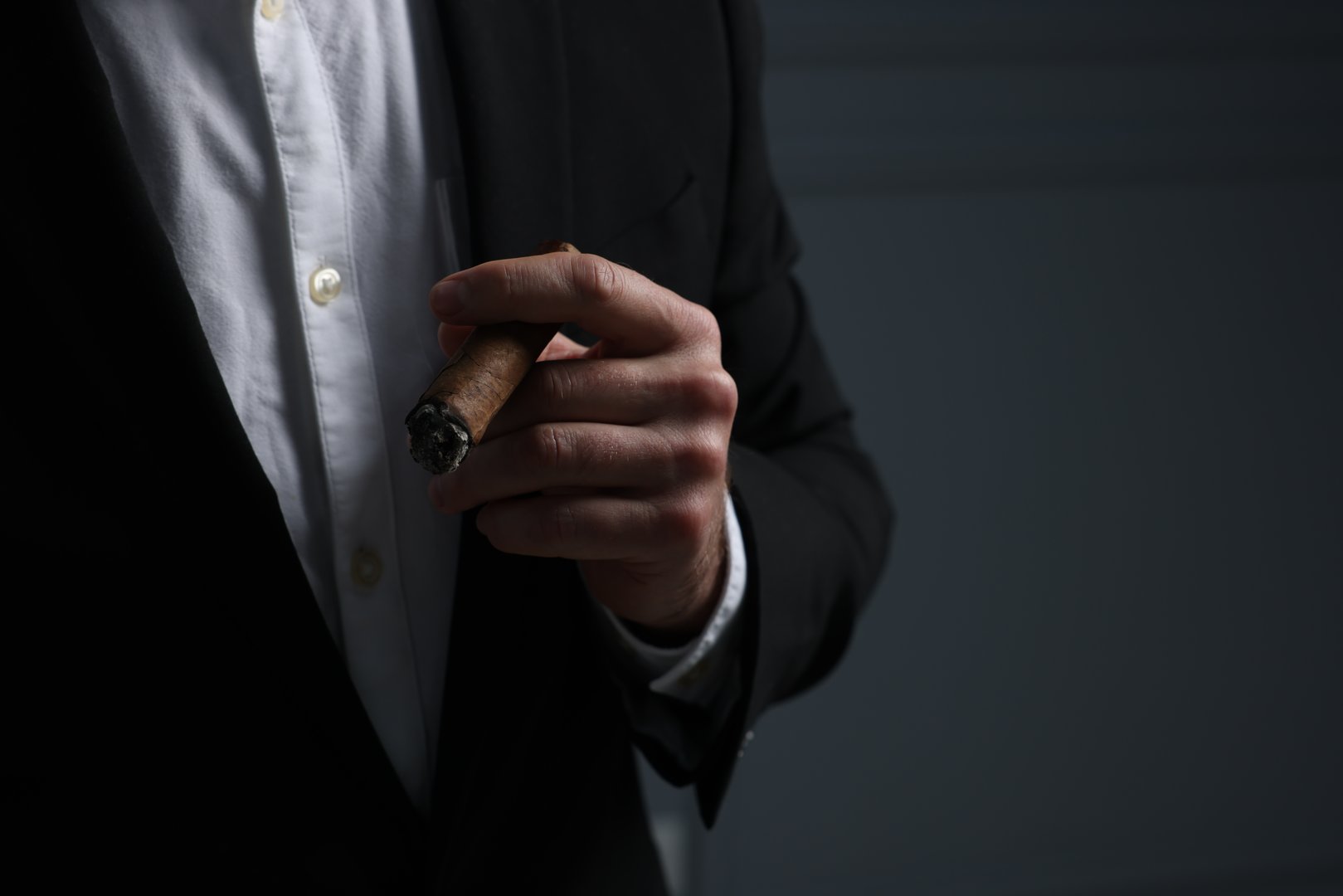 Man smoking cigar on dark grey background, closeup. Space for text