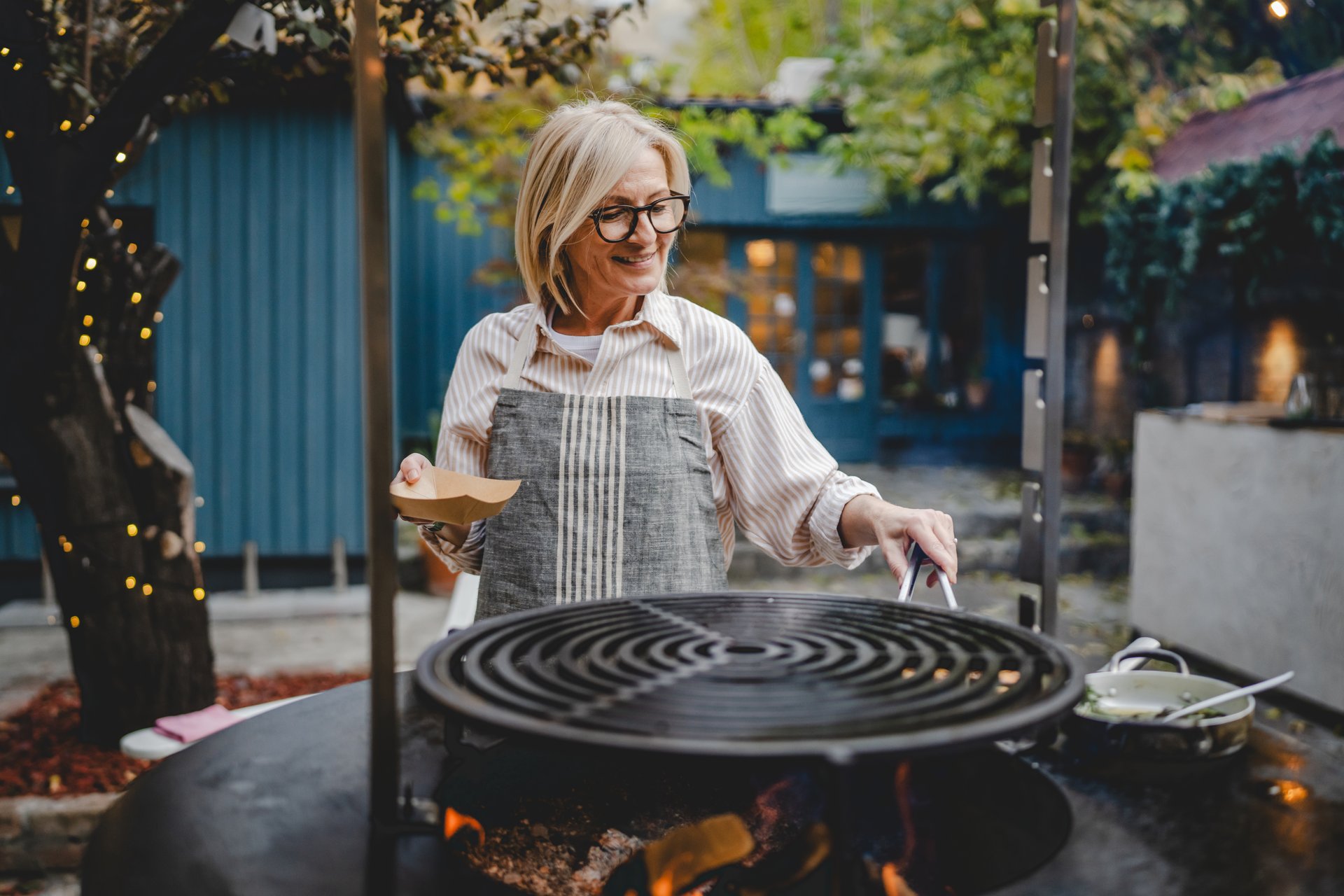 Mature senior woman waitress grilling and prepare food for guests to take away in the restaurant garden