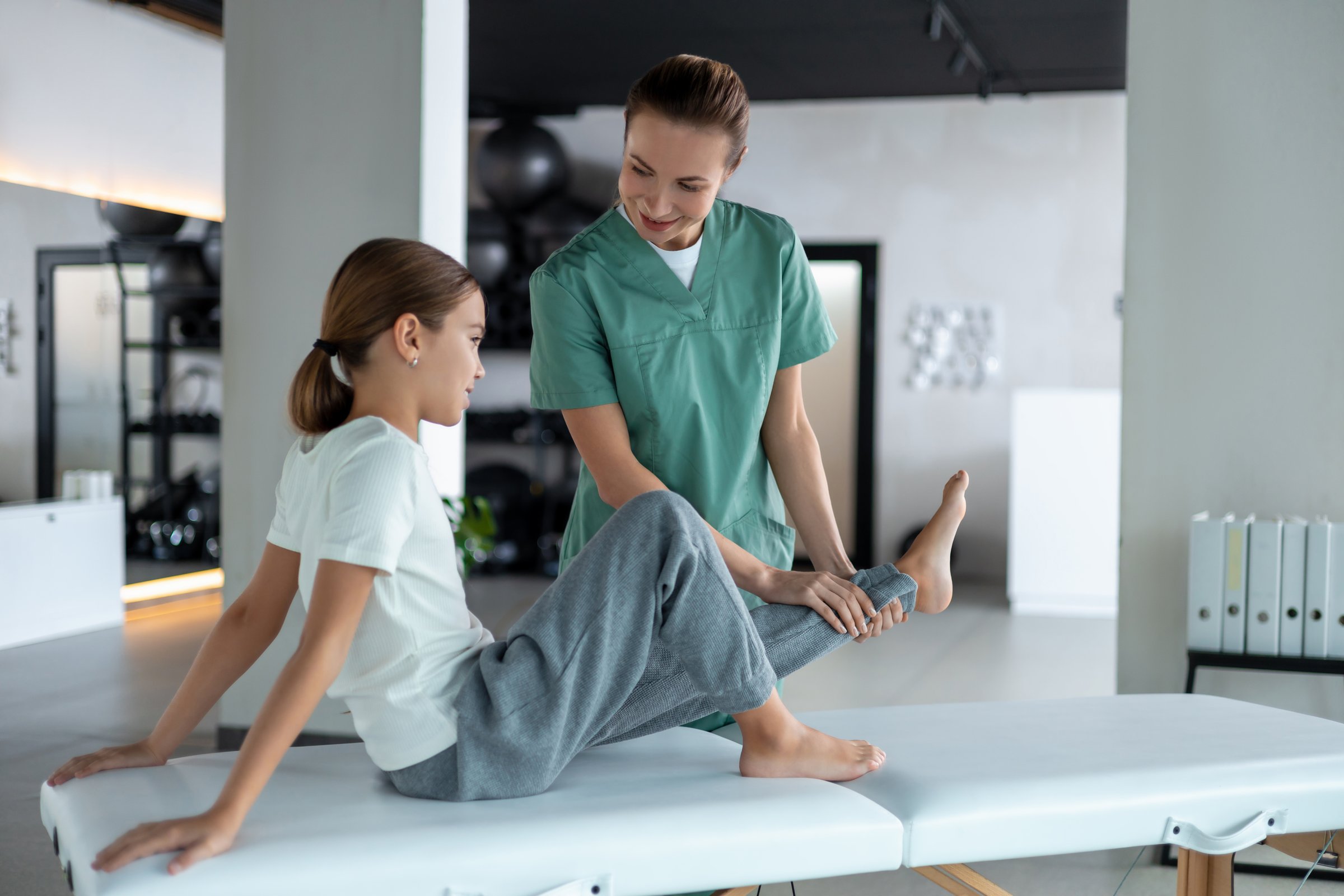 Therapist supporting child while performing active leg rehabilitation exercise in clinic