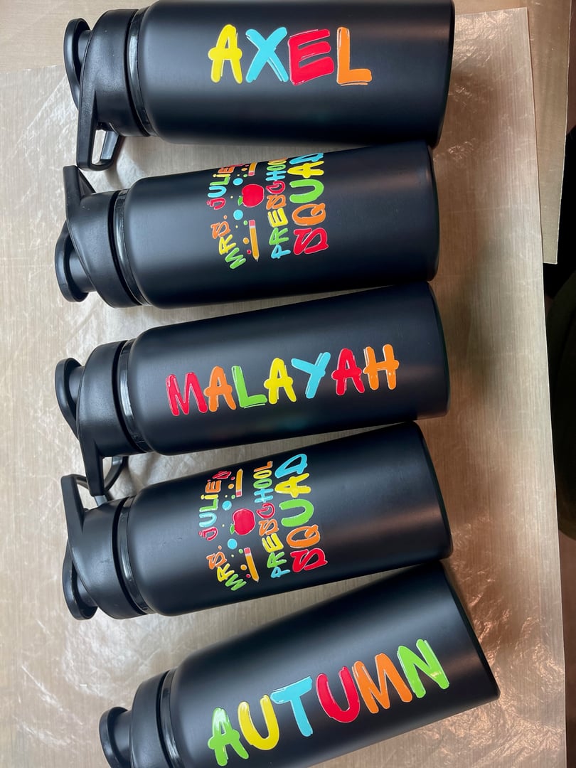 Five black water bottles with brightly colored names: Axel, Malayah, and Autumn, featuring playful fonts and designs.