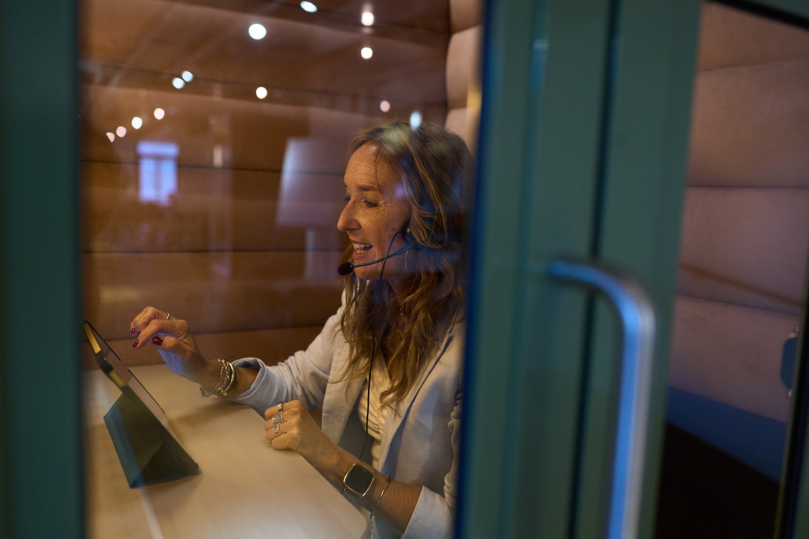Woman using a tablet and headset in an office privacy pod, making a video call for remote work or customer service