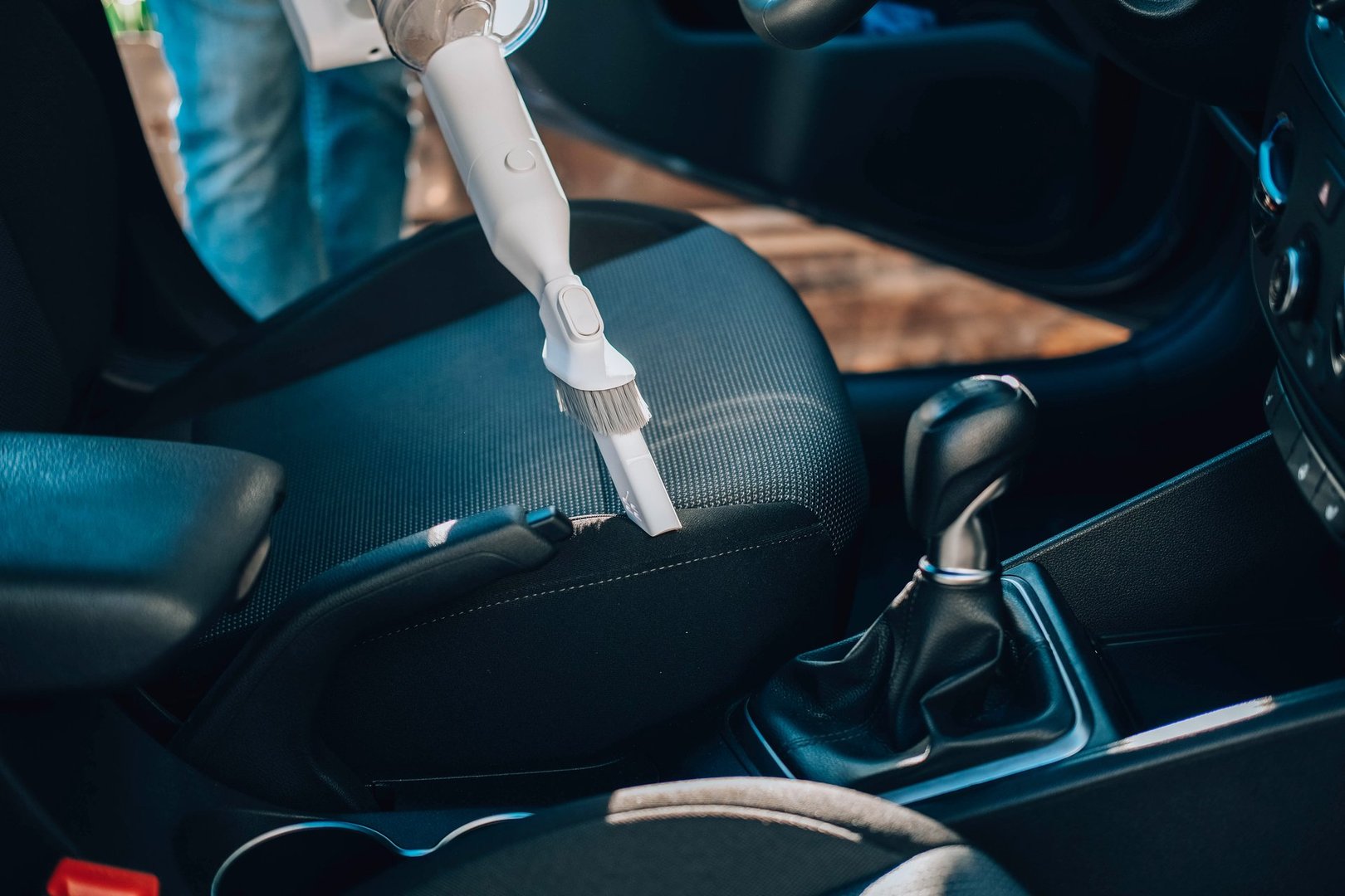 Close-up of a man vacuuming a car seat. The hand holds a cordless vacuum cleaner and cleans the interior of the car.