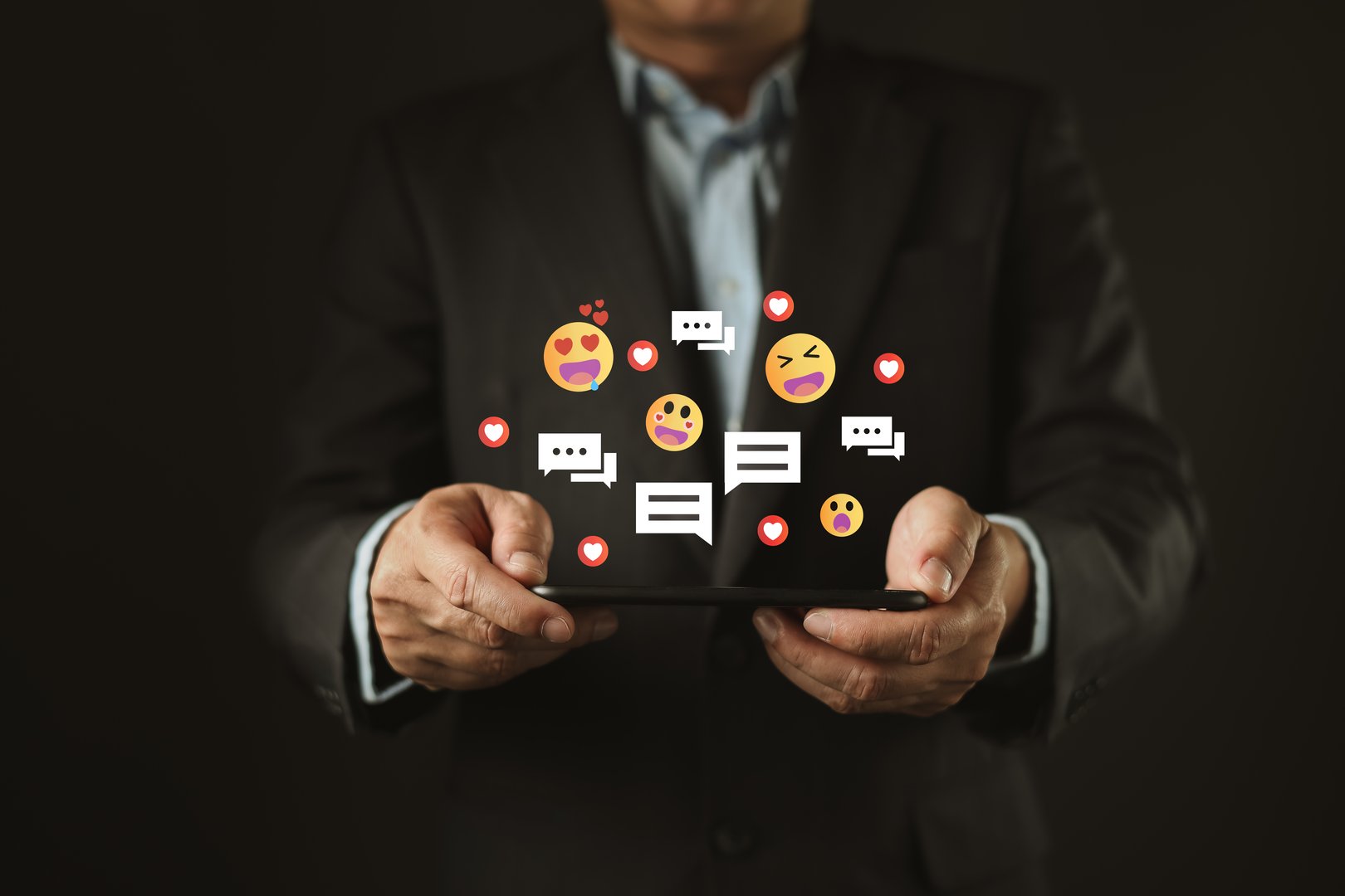 A businessman uses a tablet while various digital emojis and speech bubbles float above, symbol social media interaction, mobile messaging, emotional engagement, and real-time communication online.
