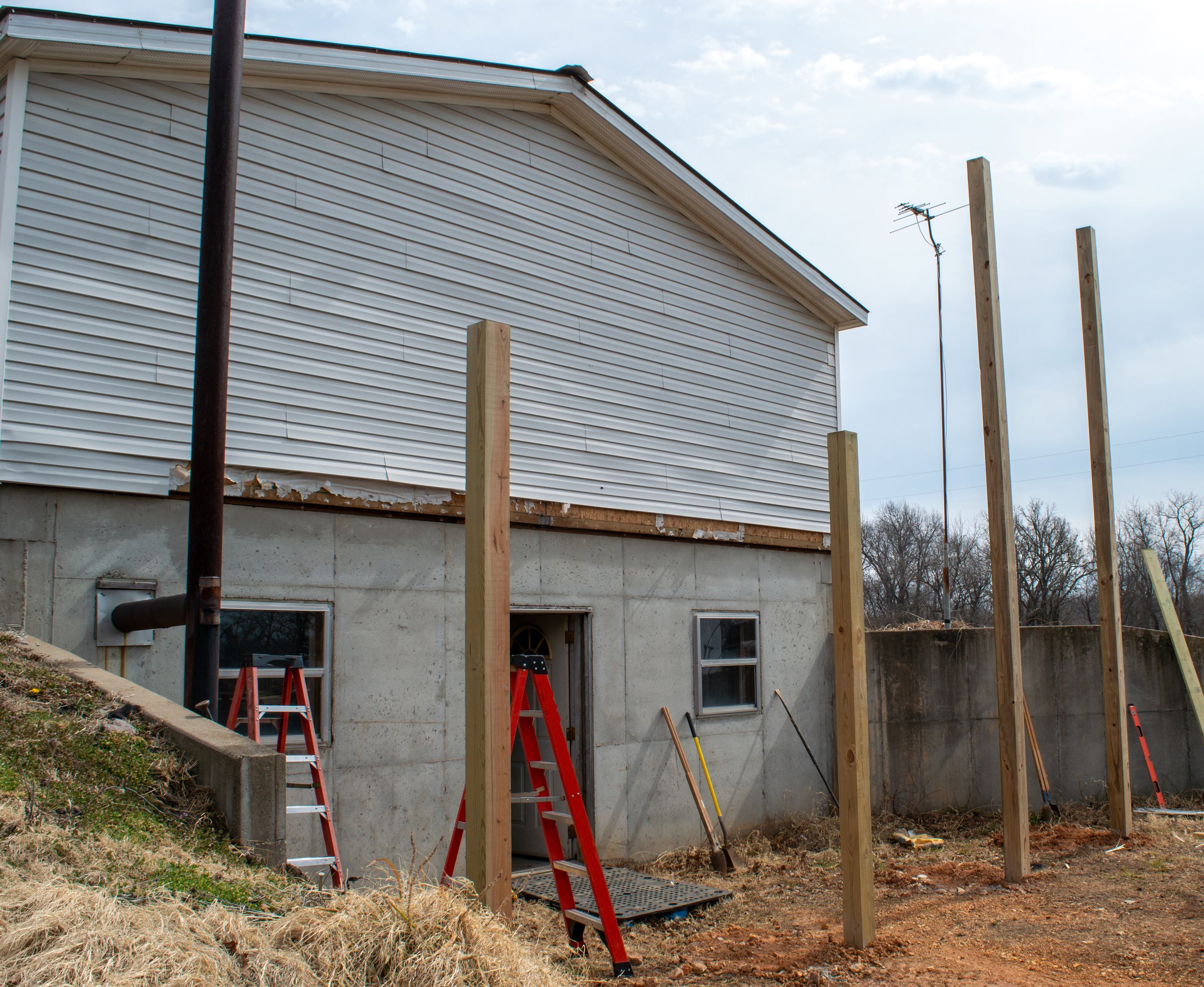 Holes have been dug and the big wooden poles have been set in the ground. The construction of a new room on the end of this home will begin soon.