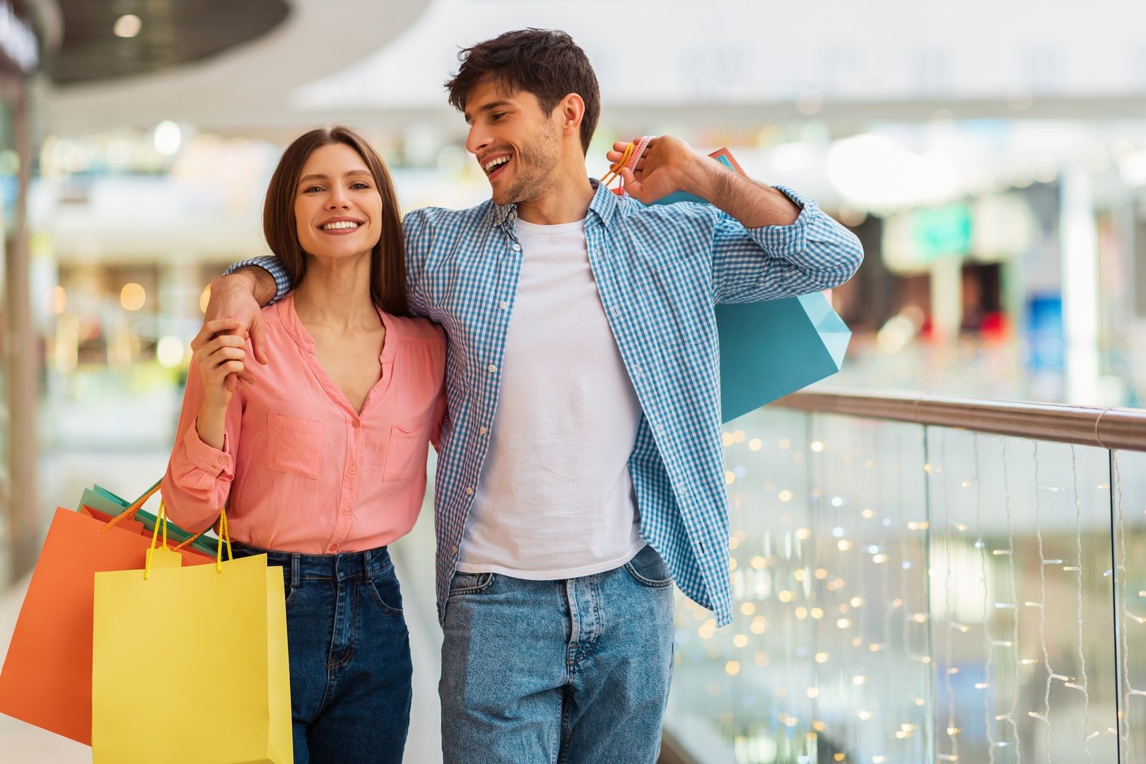 Happy Couple Hugging Doing Shopping Walking And Carrying Shopper Bags Enjoying Weekend Together In Modern Hypermarket