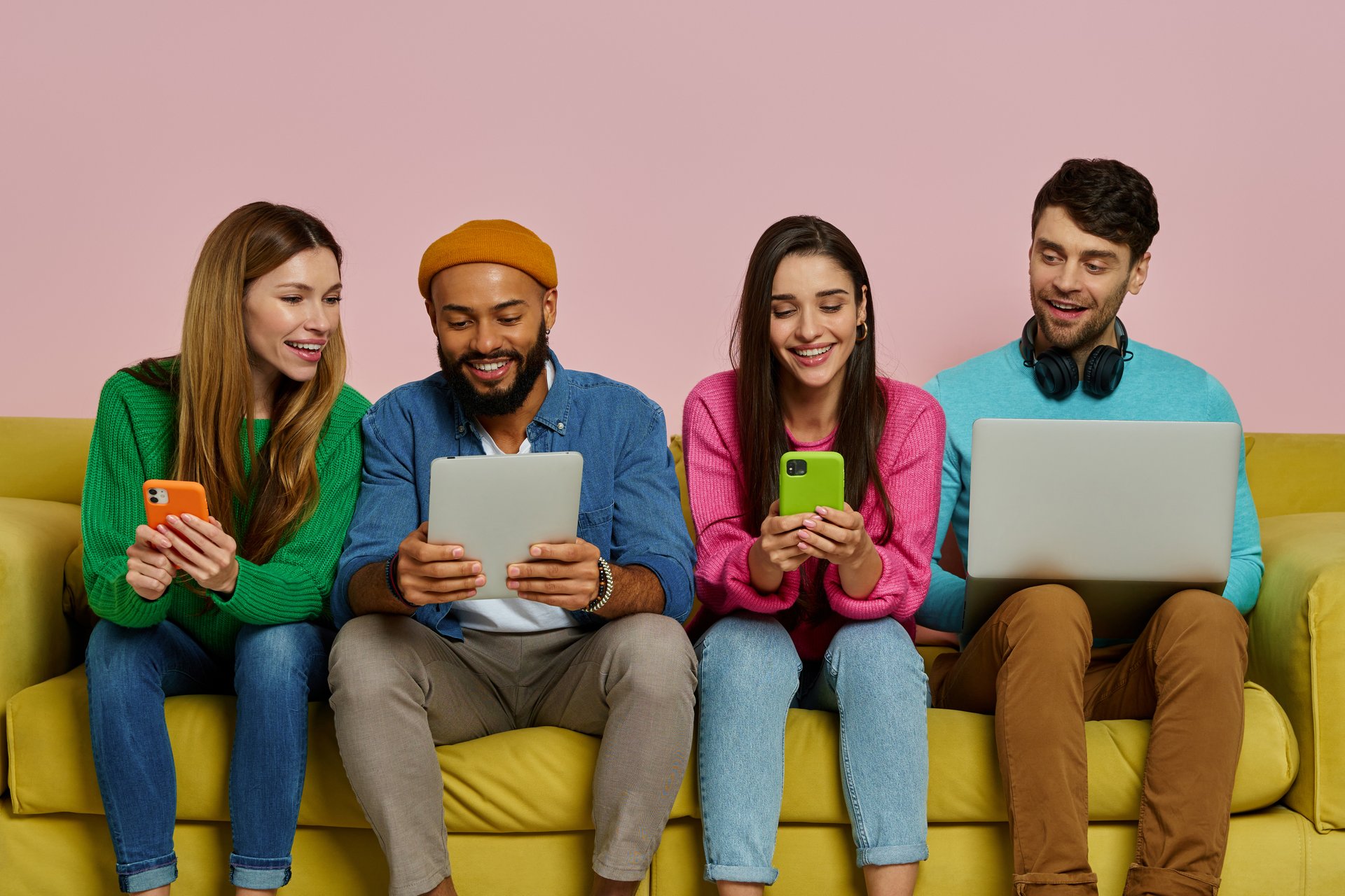 Studio shot of young people using technologies and smiling while sitting on the couch together