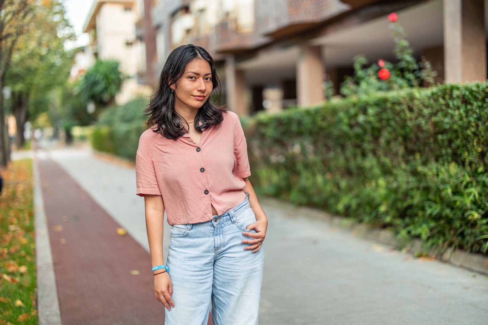 Young Asian woman standing confidently on a city sidewalk, posing casually with one hand in her pocket, enjoying an urban lifestyle moment outdoors during the day
