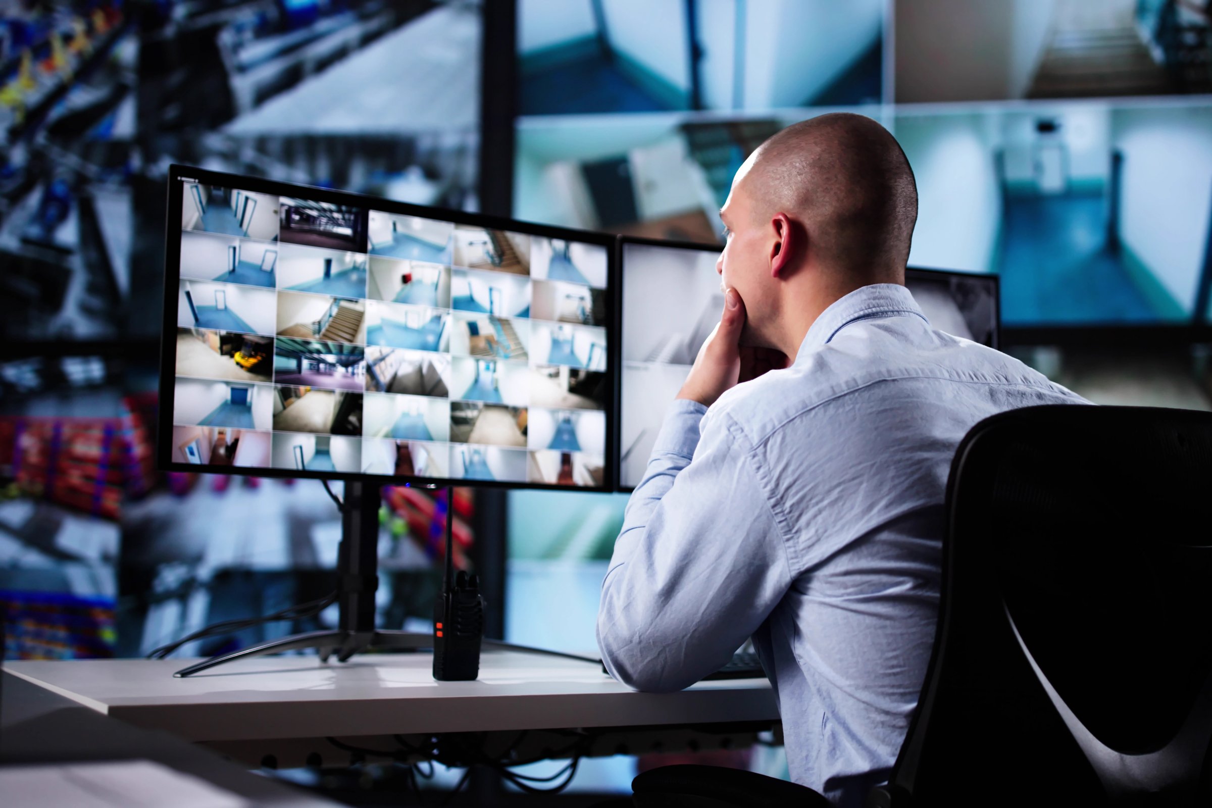 Rear View Of A Man In Control Room Monitoring Multiple CCTV Footage
