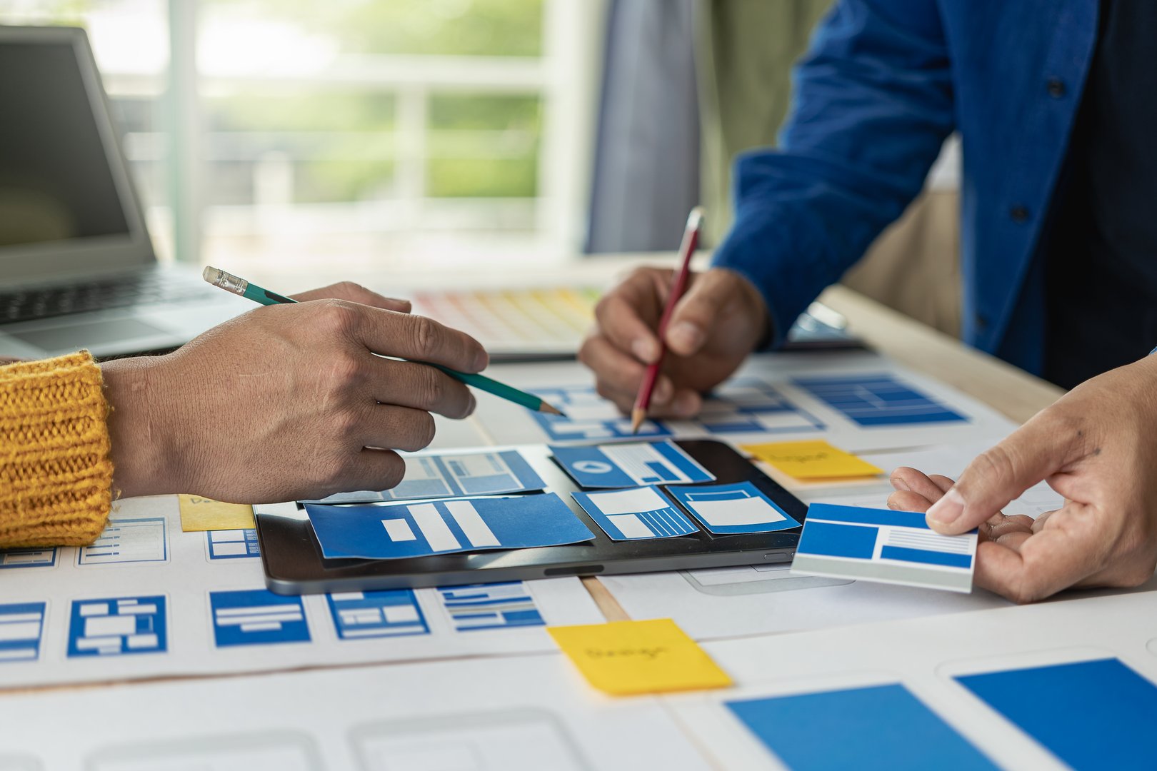 A team of web designers are working together to develop a mobile responsive website with UI/UX front end design concepts. A team of UxUi developers are working together at a wooden workbench.