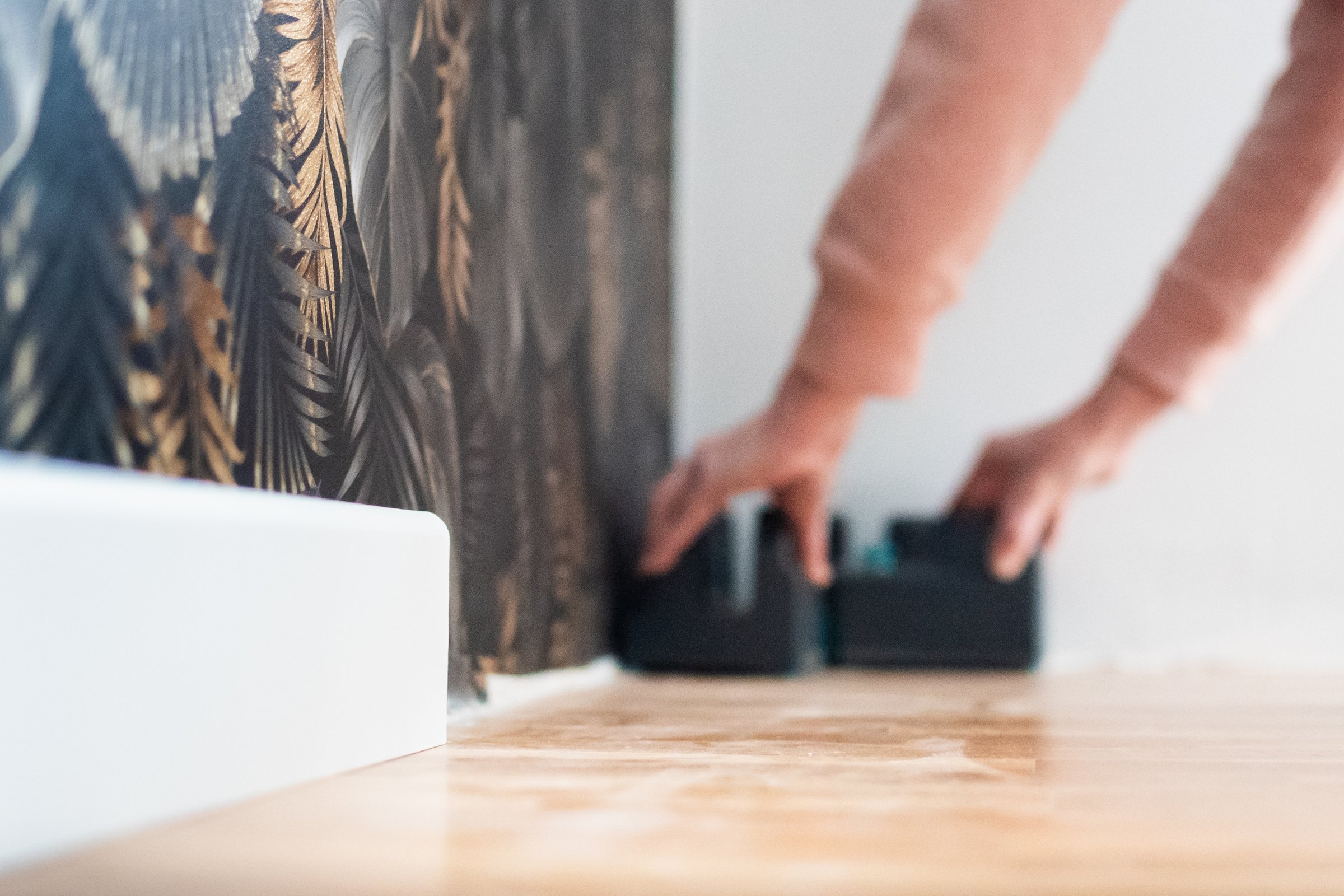 Hands carefully aligning patterned wallpaper against a wall in a home improvement project