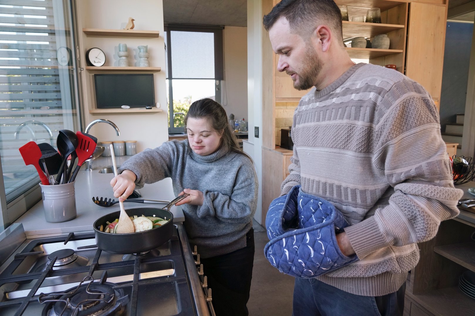Man assisting woman with Down Syndrome frying vegetables in kitchen