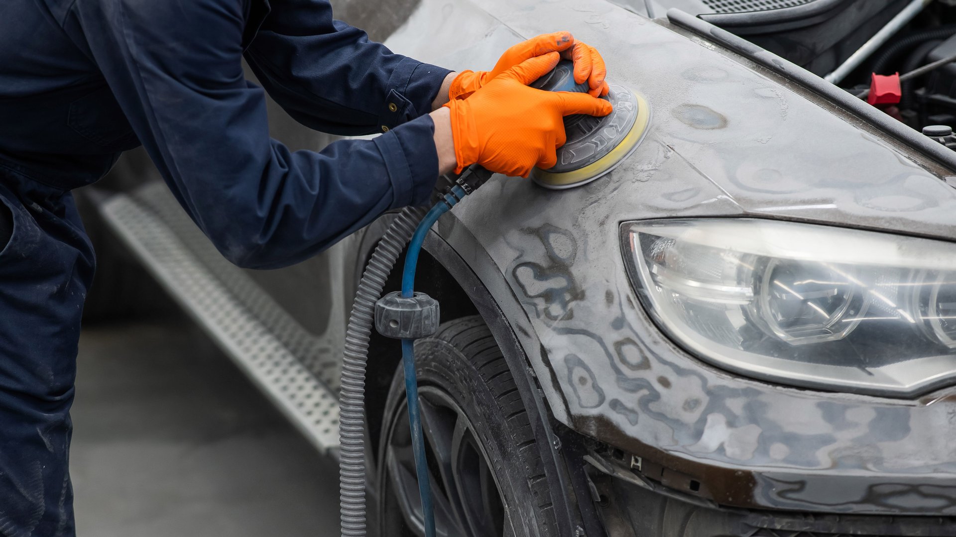 A mechanic sands the putty on a car body with a machine. Repair after an accident