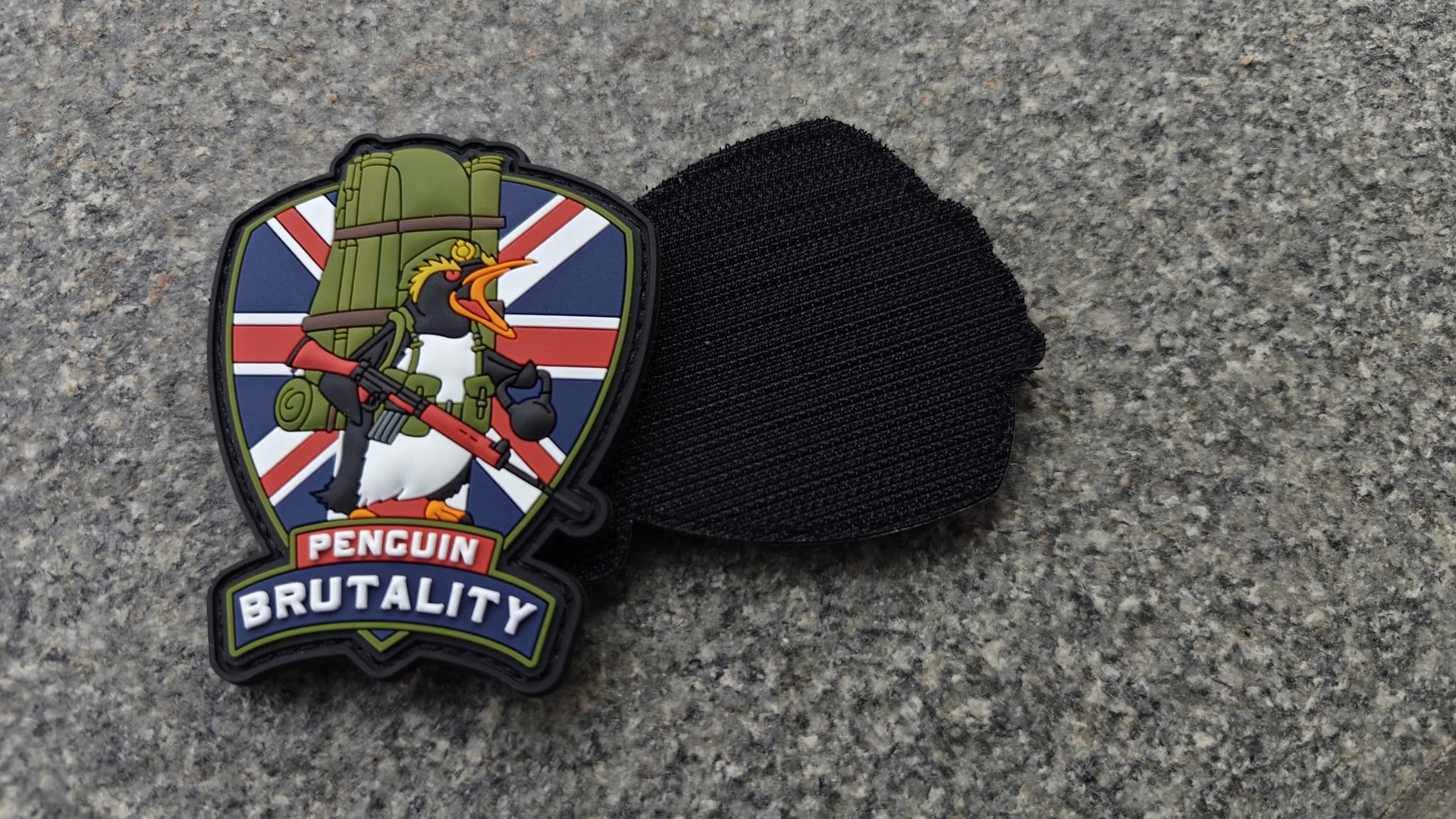 A patch depicting a penguin with a rocket launcher, labeled Penguin Brutality, on a Union Jack background, next to a black backing.