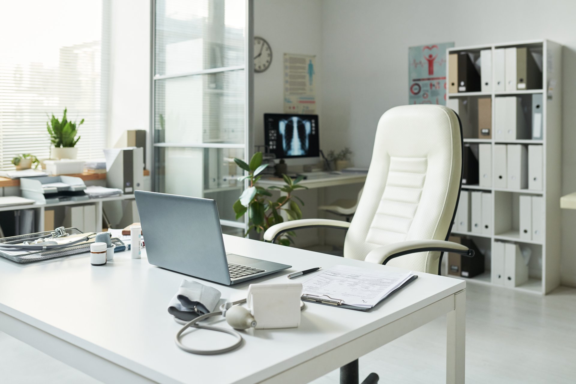 Empty medical office showing desk with laptop, blood pressure monitor, clipboard, prescription bottles, stethoscope, indicating preparation for patient with diabetes consultation