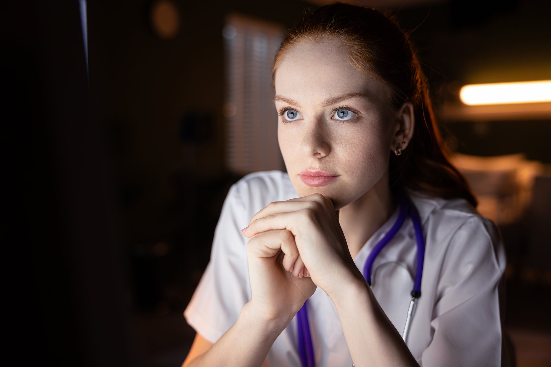 Red-haired doctor in white coat using computer in hospital room.
