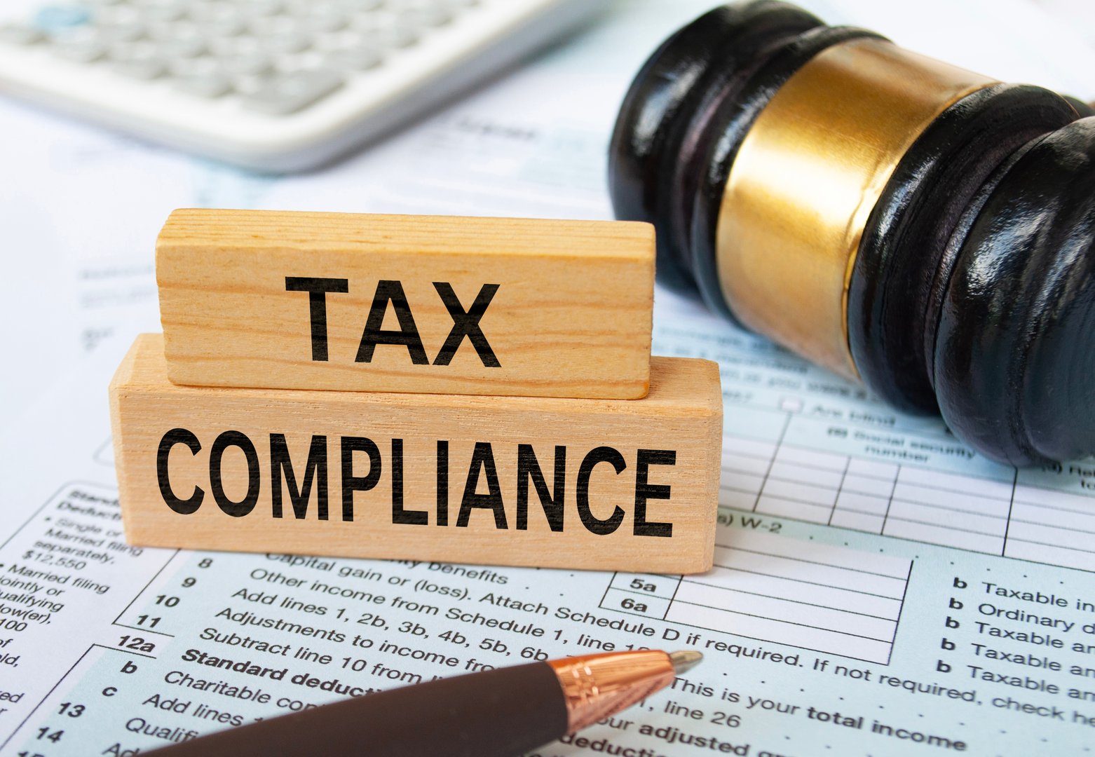 Tax compliance text on wooden blocks with tax form, gavel and calculator background. Taxation concept.