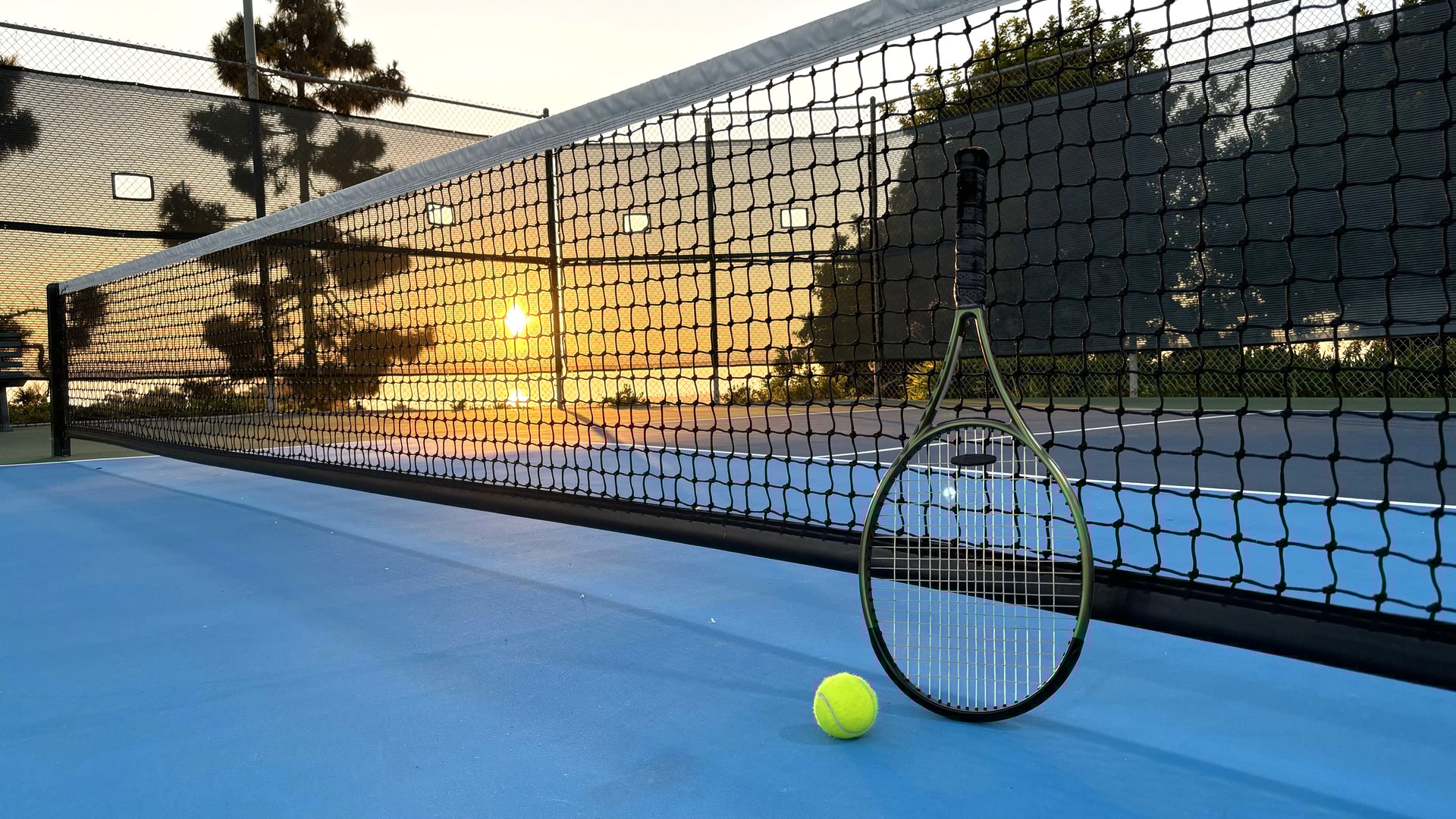 Sun setting over the tennis court. Tennis racquet and tennis ball on the empty tennis court. Low angle view
