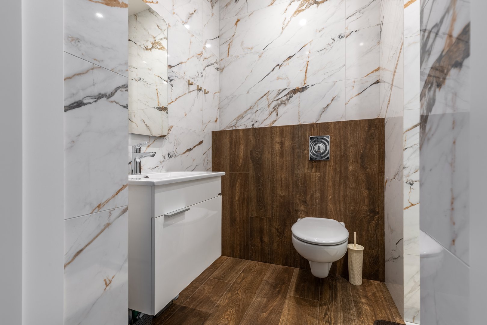 A stylish bathroom featuring marble walls, wooden paneling, a floating vanity, a wall-mounted toilet, and bright lighting, creating an elegant modern design.
