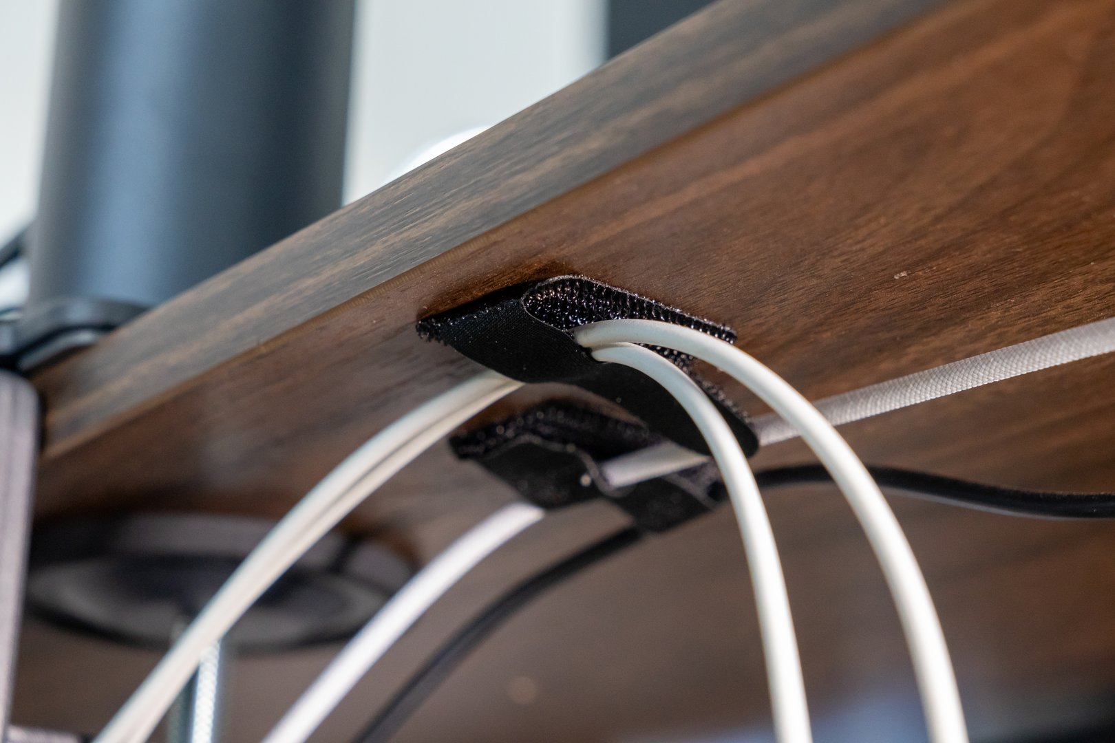 cable management under wooden desk using black velcro straps, showcasing organized wiring setup for efficient workspace arrangement, close-up view