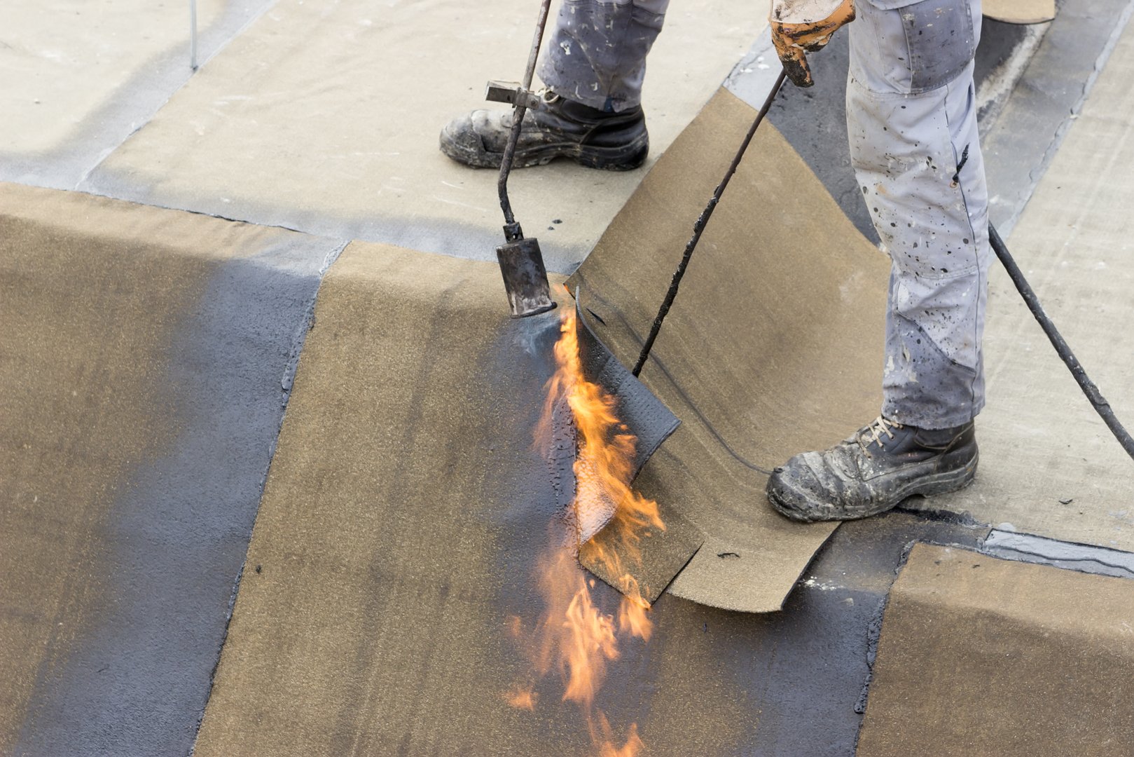 Insulation worker with propane blowtorch at floor slab insulation work. Worker heating and melting roll of bitumen roll.