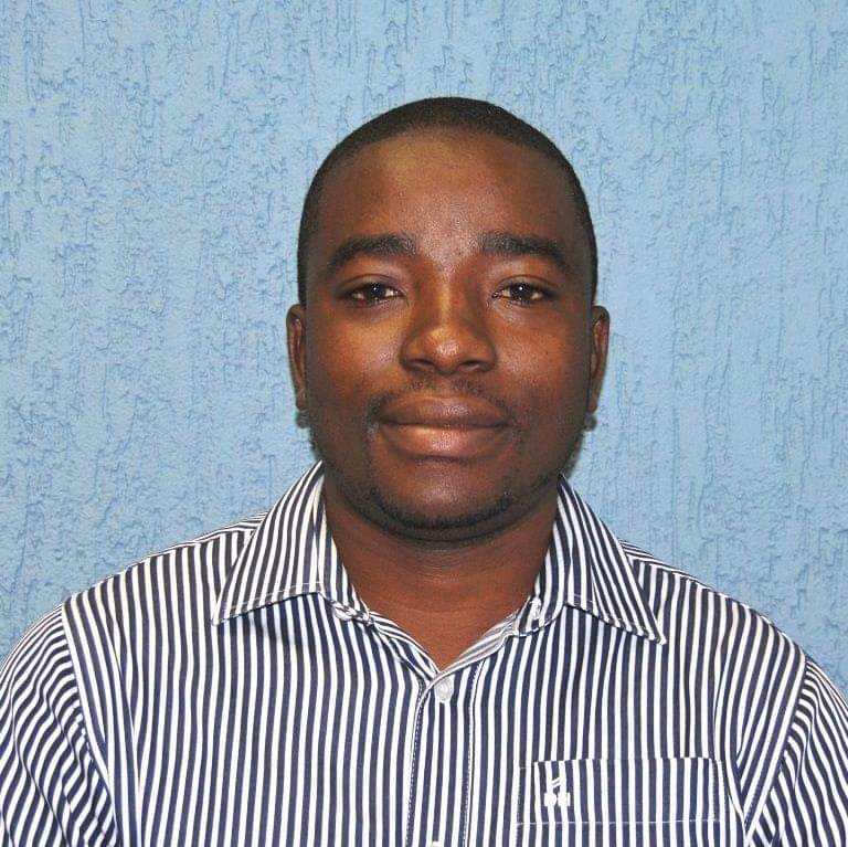 Portrait of a man in a striped shirt against a textured blue background, facing the camera with a neutral expression.