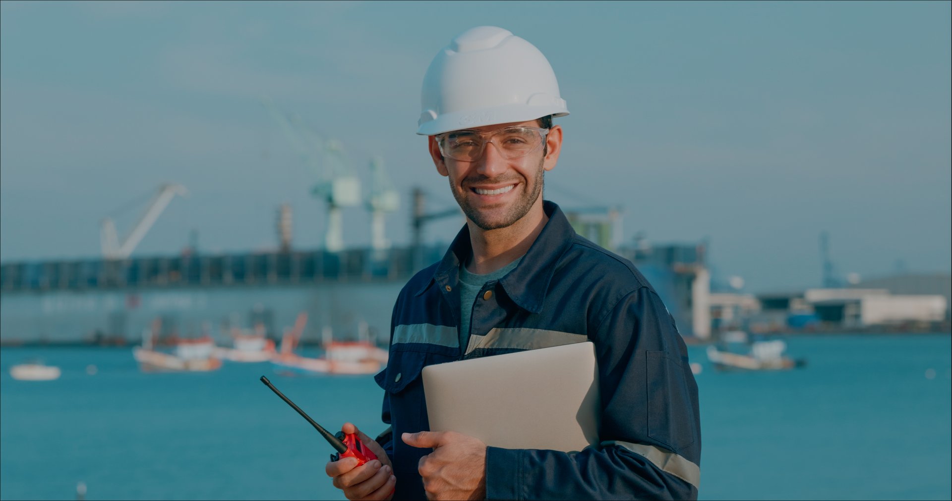 Portrait maintenance engineer smiling handhold computer notebook after meeting a plan to repair or Rebuild a large bulk ship damaged via an application and using Artificial Intelligence (AI) to research data with the resulting design rebuild on a laptop at a Commercial Shipyard.