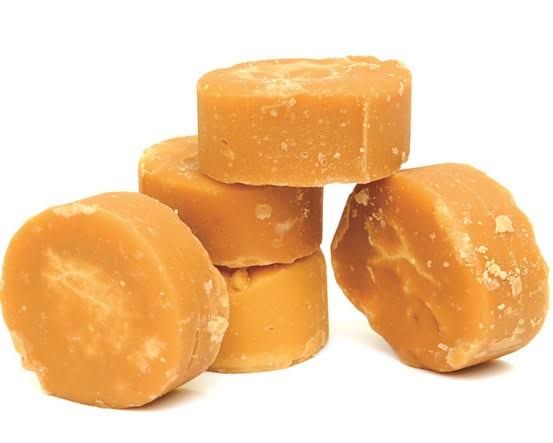 Stack of round, brown sugarcane jaggery discs with a rough texture on a white background.