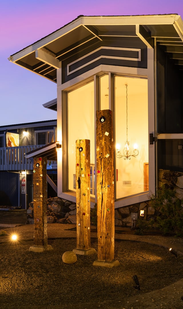 Wooden sculptures with embedded stones lit by spotlights outside a modern building at dusk.