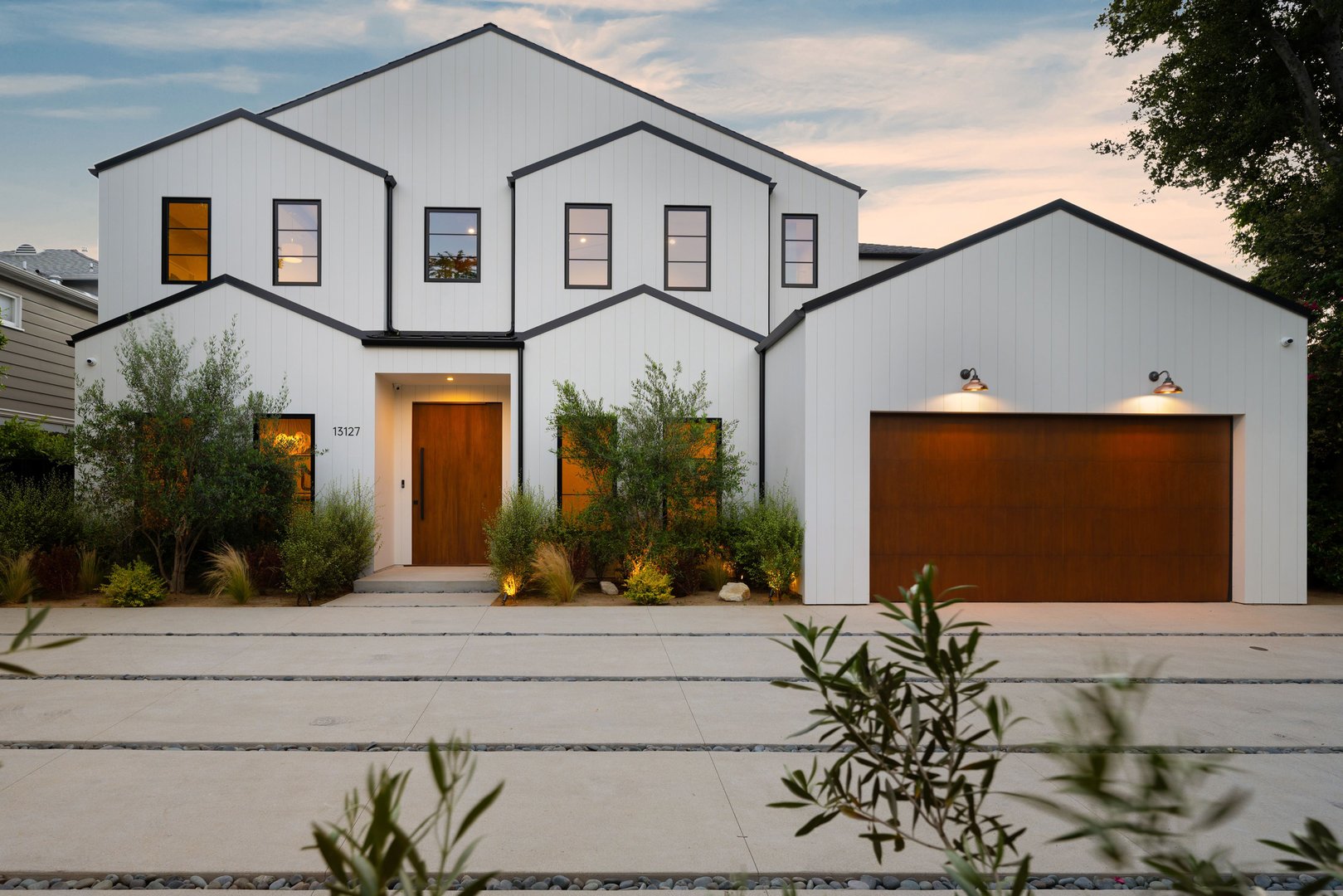 Modern white house exterior with wooden accents and landscaped front yard at dusk.