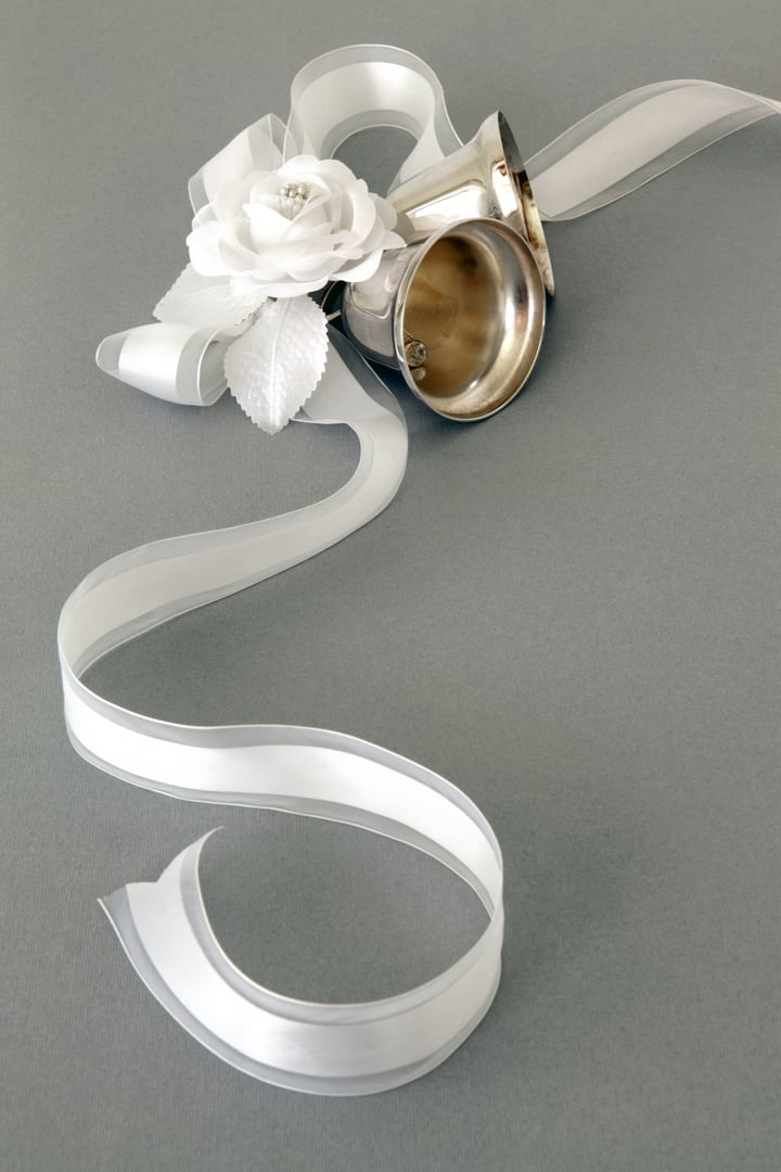 Silver wedding bells tied with a white ribbon and adorned with pearls and flowers on a silver background