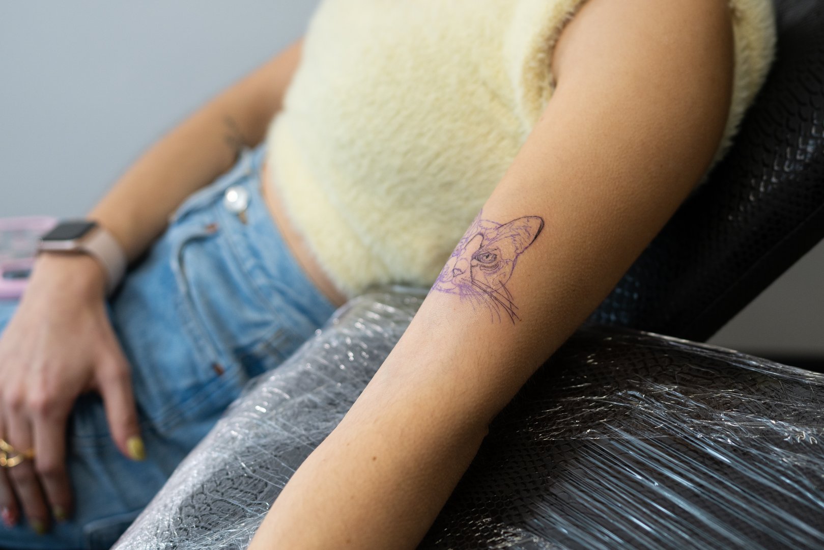 Female client getting vibrant cat tattoo on arm inside professional tattoo studio, capturing personal connection through intricate body art design with meticulous detail and emotional significance