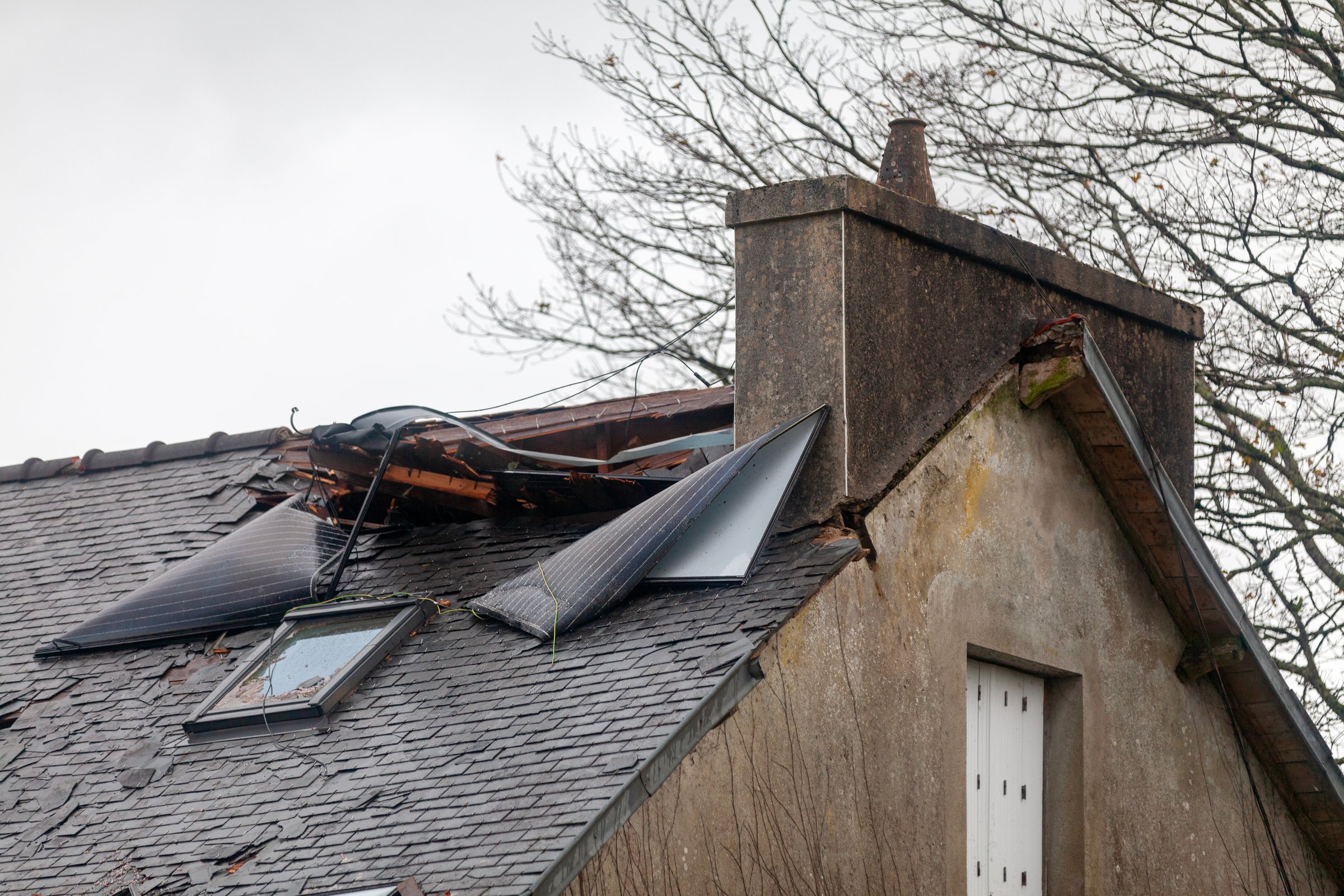 Roof of a house damaged after the solar panels of the building opposite it were torn off and traveled about 50 meters at 106 mph during an autumn storm, ending up embedded near the chimney.