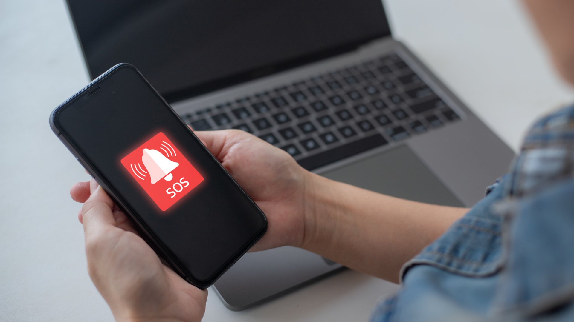 Close-up hand holding a smartphone with the SOS emergency alert app icon on screen. Concept of mobile safety, urgent help, security system, healthcare emergency, and digital technology.