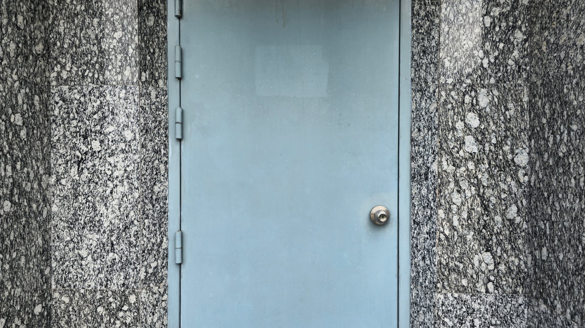 The blue door outside the building, the building walls are covered with shiny black granite tiles, which is the background of the building walls.