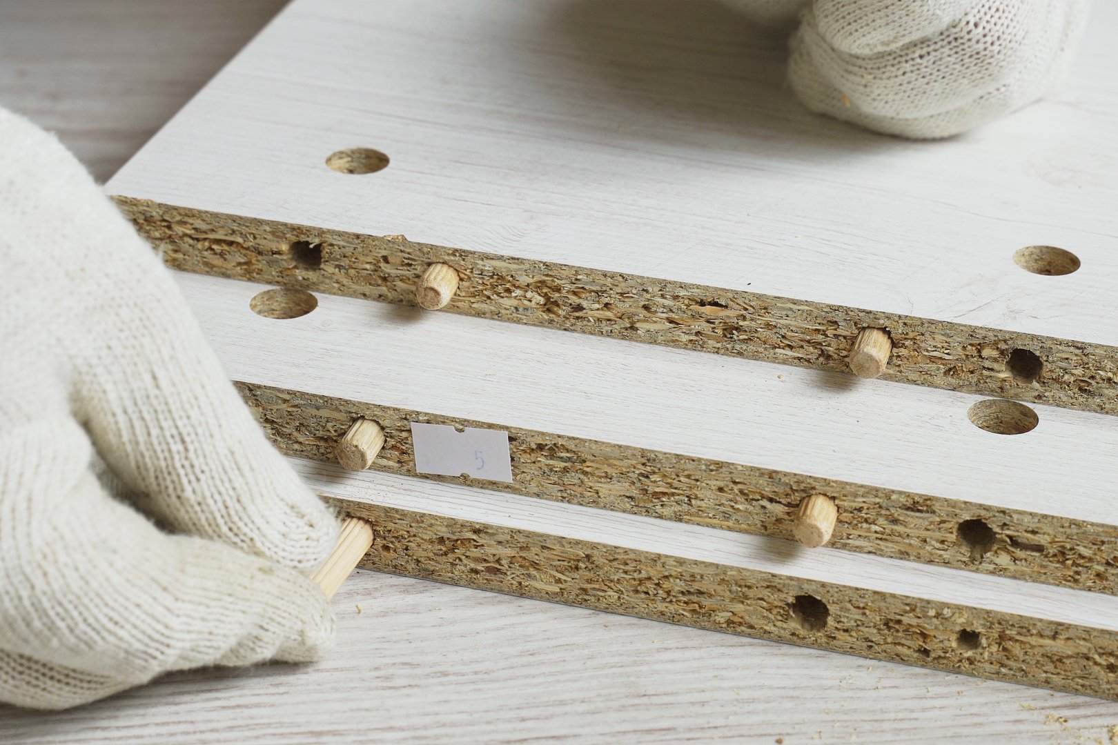 Furniture assembly. A worker inserts wooden dowels by hand into the holes of cabinet furniture parts. Close-up.