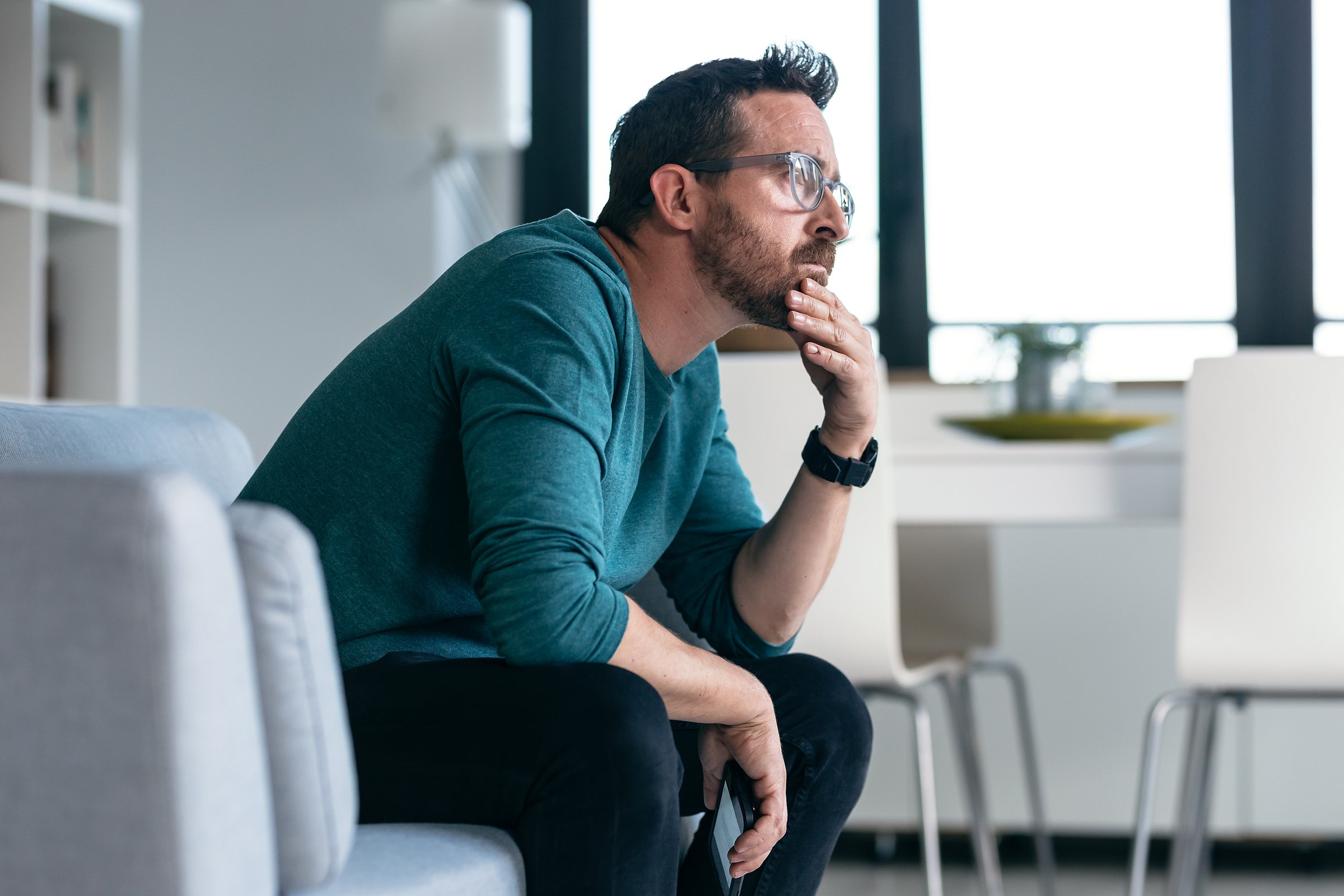 Shot of worried mature man thinking about what he has read on his mobile phone while sitting on the couch at home