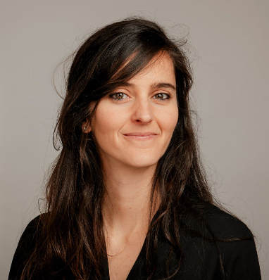 A woman with long dark hair and a black top smiling, set against a plain light background.