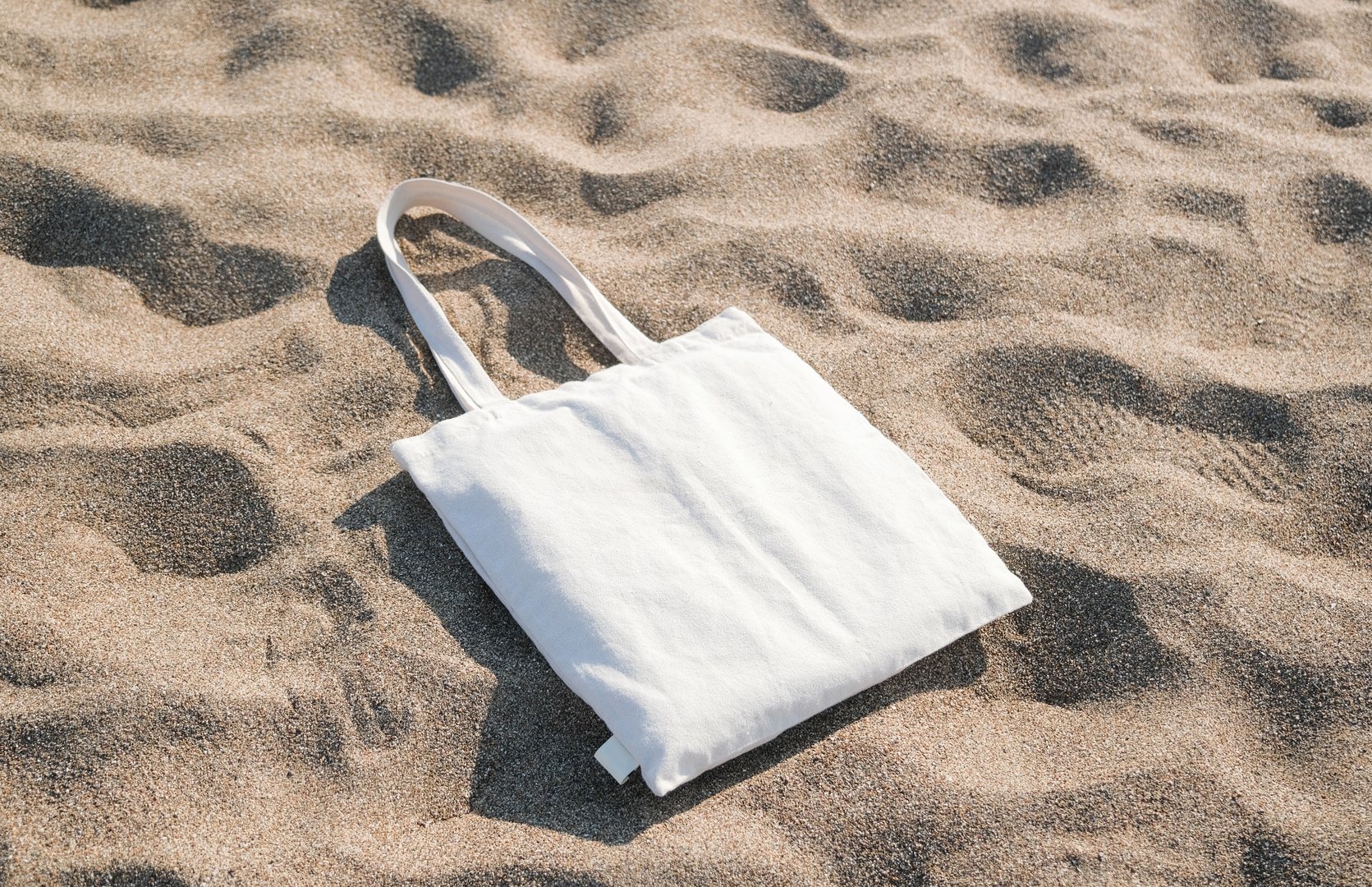 White cotton or mesh bag on beach sand background. Zero waste, no plastic, eco friendly shopping, recycling concept. Blank mockup shopper with place for artwork or text