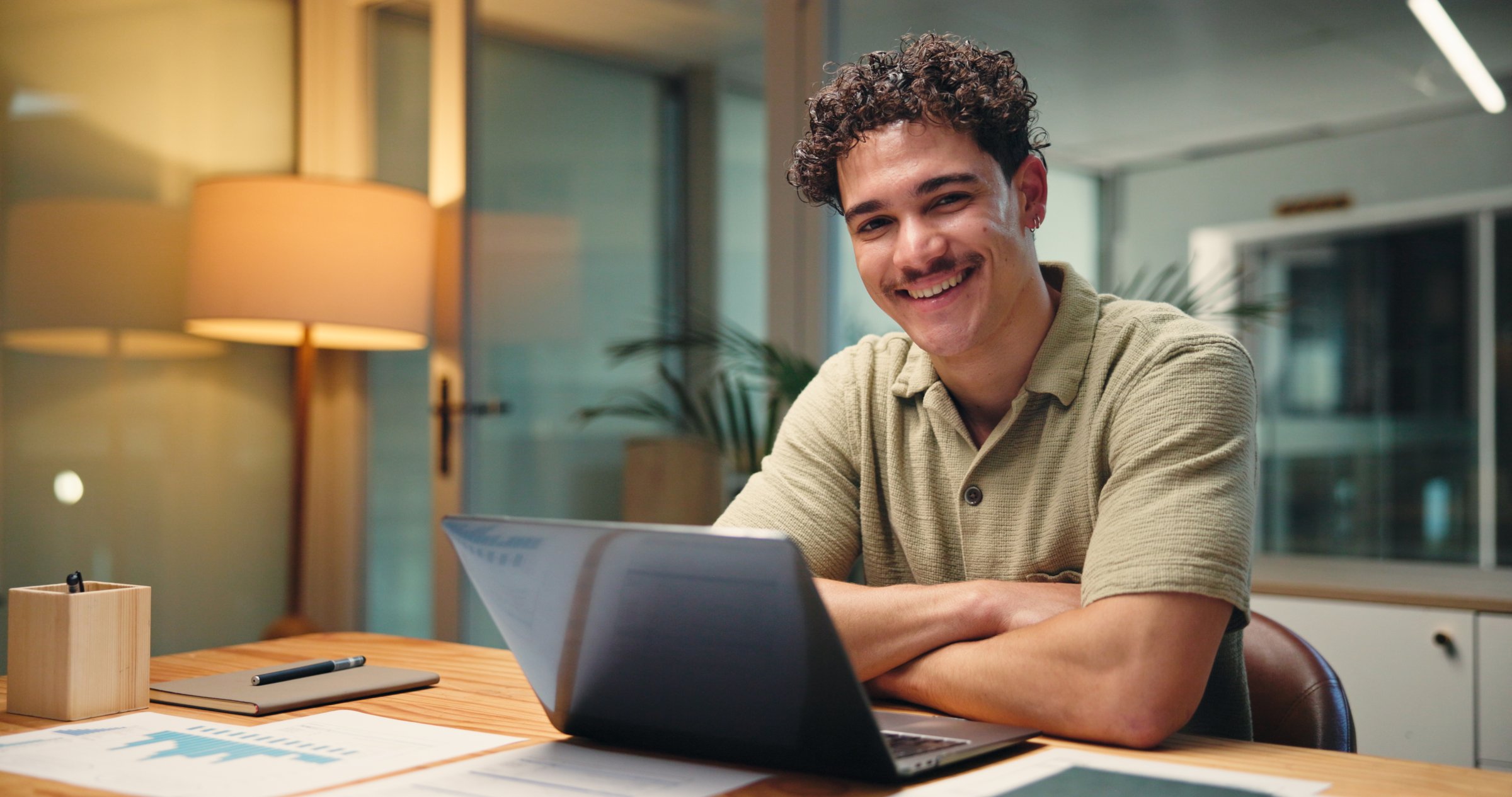Laptop, portrait and smile of business man in office at night for social media analytics. Arms crossed, computer and statistics with happy employee at workplace desk for evening deadline or research
