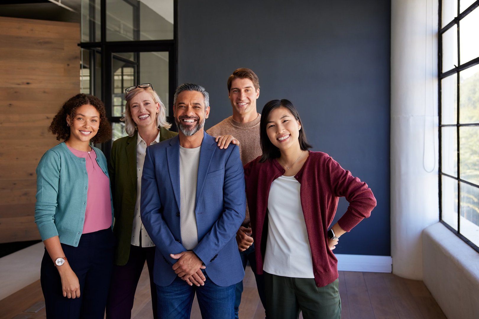 Group of multiethnic businesswomen and businessmen standing together in a bright office. Confident business team posing for a portrait together. Business group of colleagues looking at camera, embodying unity and collaboration.