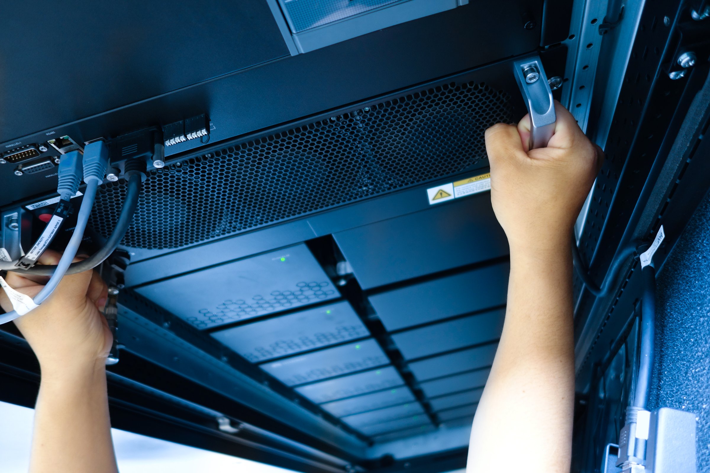 A technician adjusts hardware in a server rack, ensuring optimal performance and connectivity. Cables are managed meticulously in a busy data center environment.
