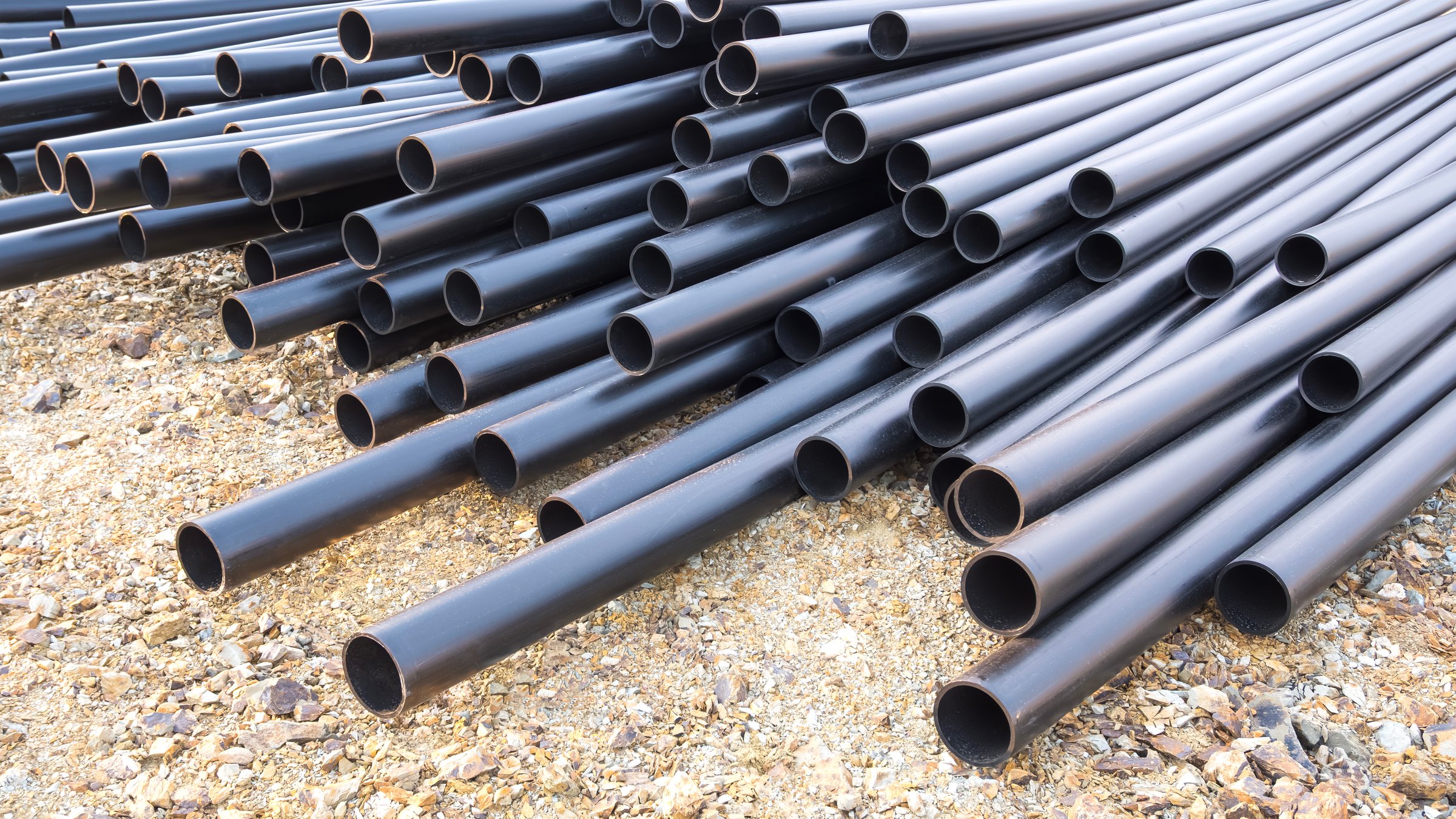Pile of many HDPE conduit pipes on the ground for underground electrical wiring in industrial factory building construction site