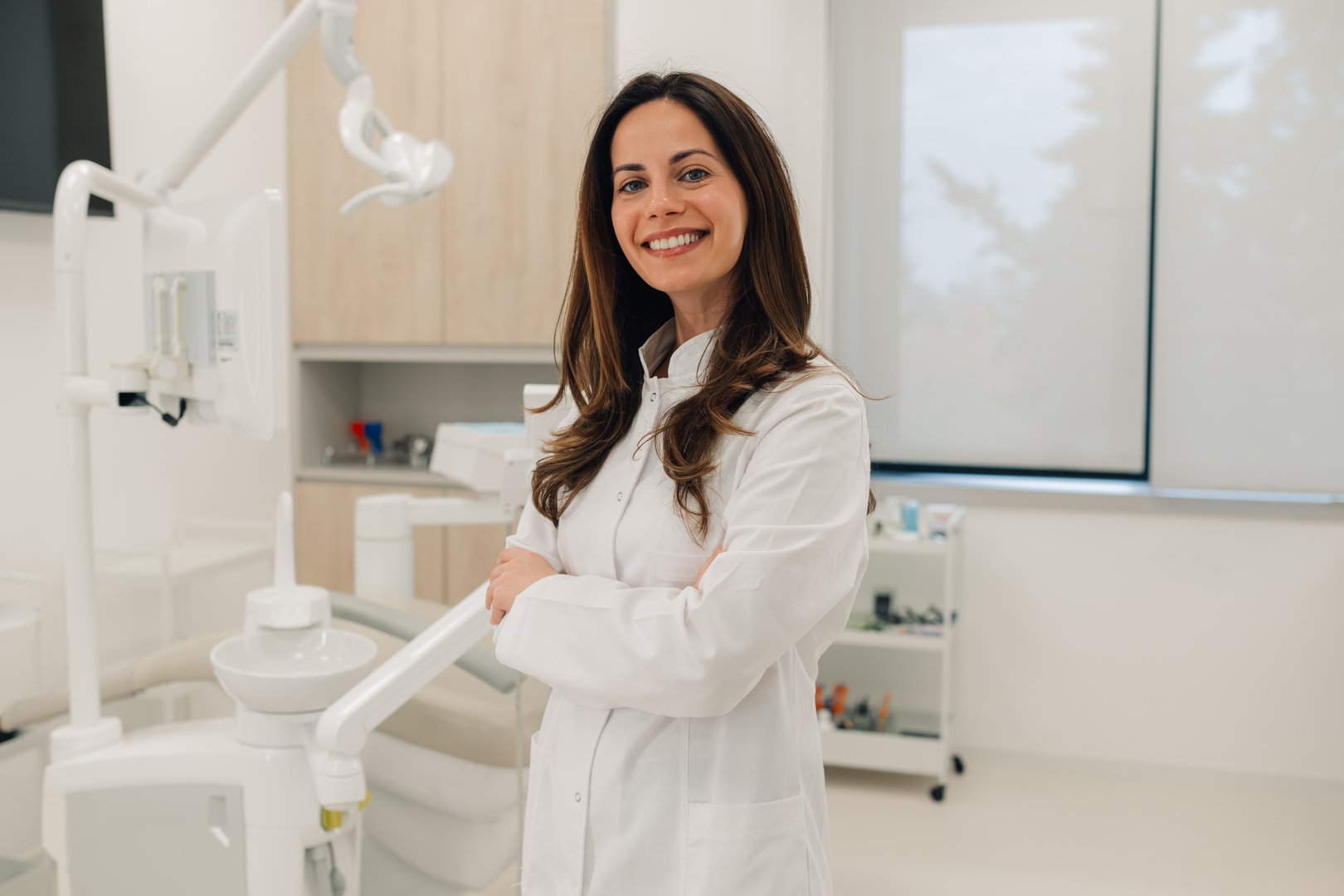 Confident female dentist smiling with arms crossed in her modern dental clinic