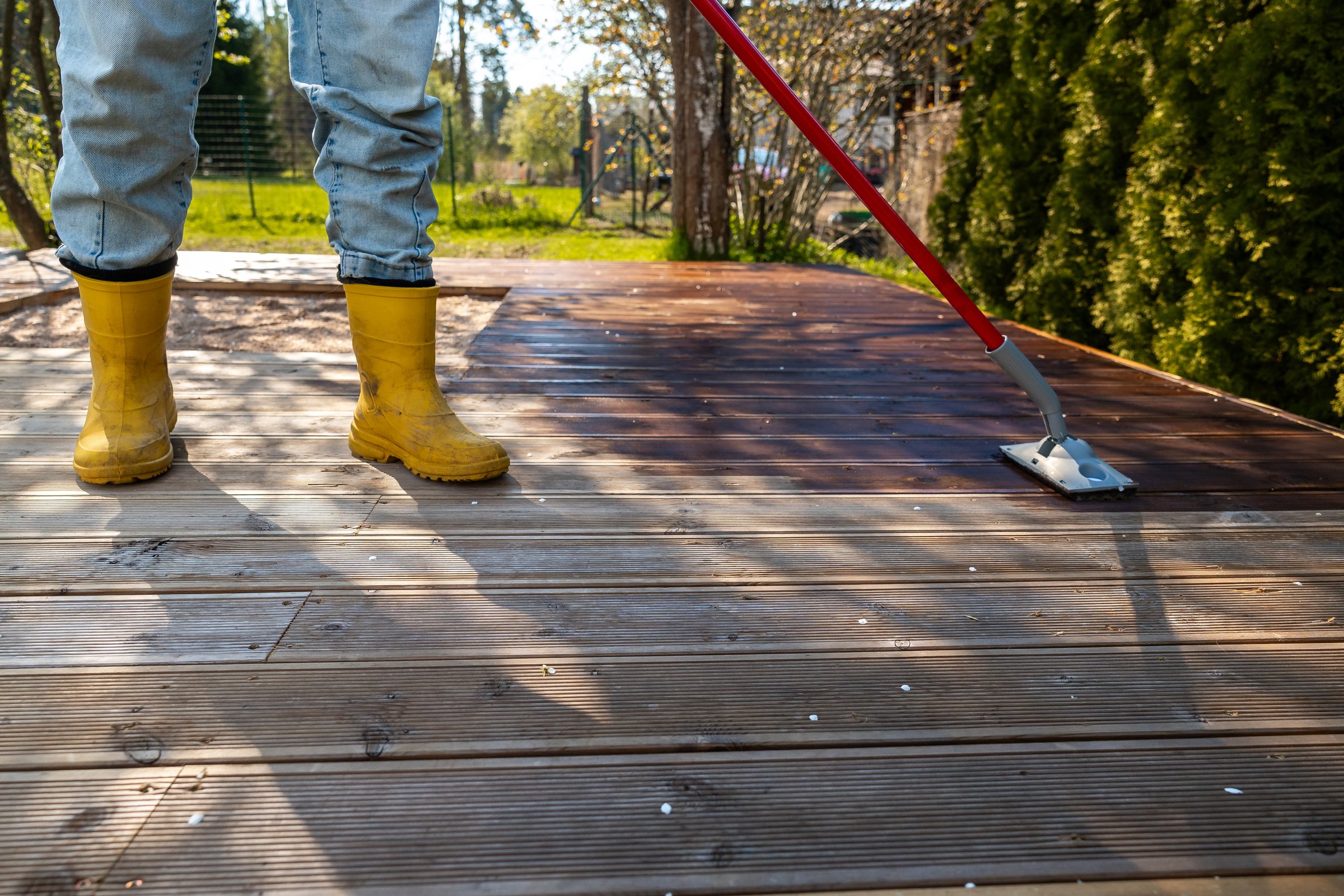 Applying stain to a wooden deck with a brush on a sunny day