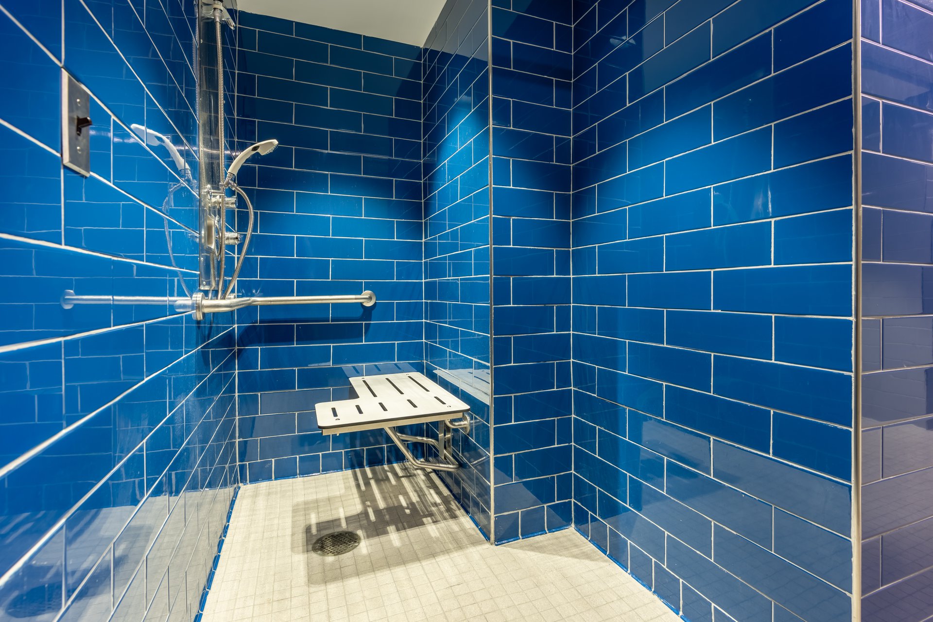 New single, private, gym locker room shower with blue tile wall, bench, and tile floor.