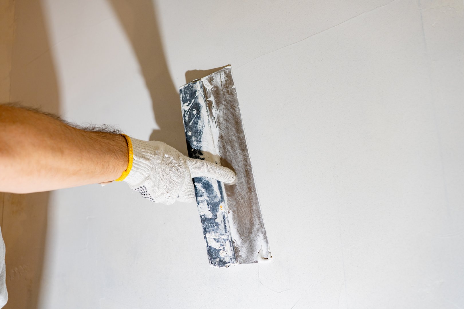 Gloved worker actively spreads white spackling compound with a finishing tool, preparing the textured wall for a final coat.