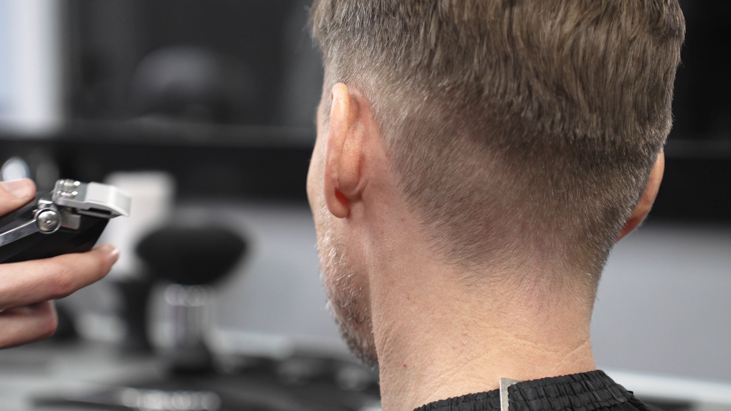 Close up of barber's hands using electric razor, creating precise haircut on male client's head in professional barbershop setting, showcasing skill and precision in men's grooming