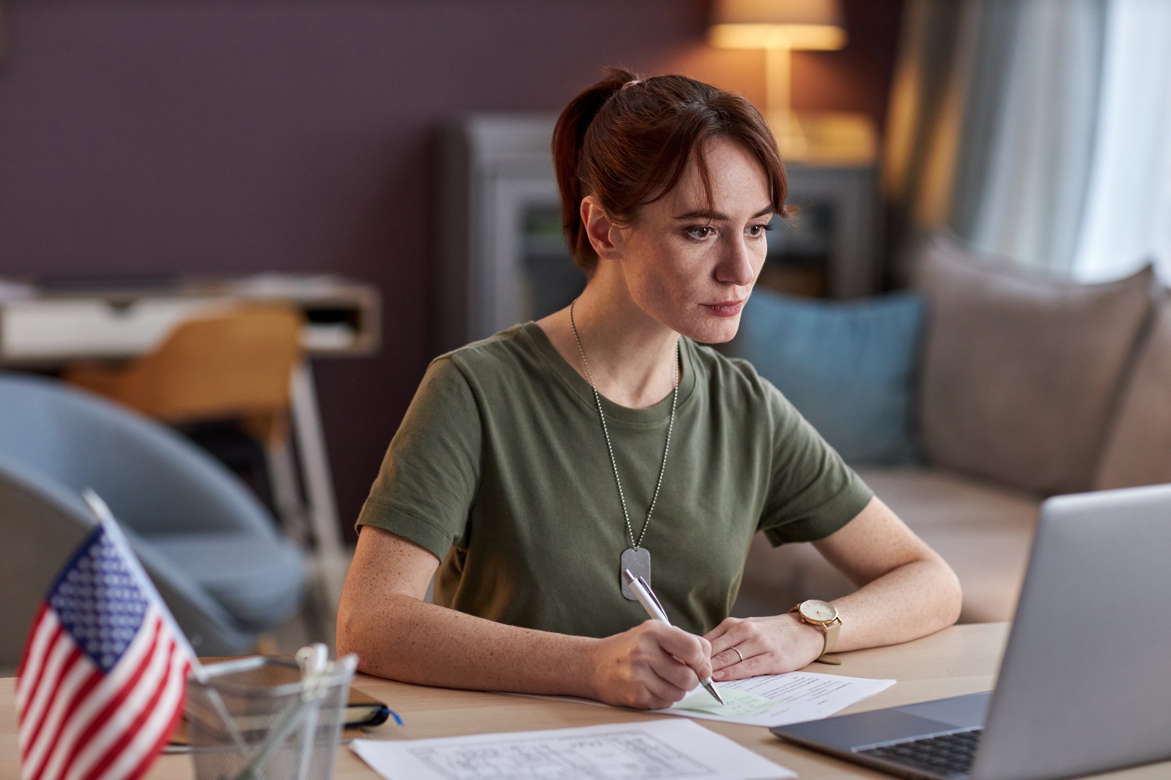 Portrait of young military woman looking at laptop screen and taking notes in online meeting